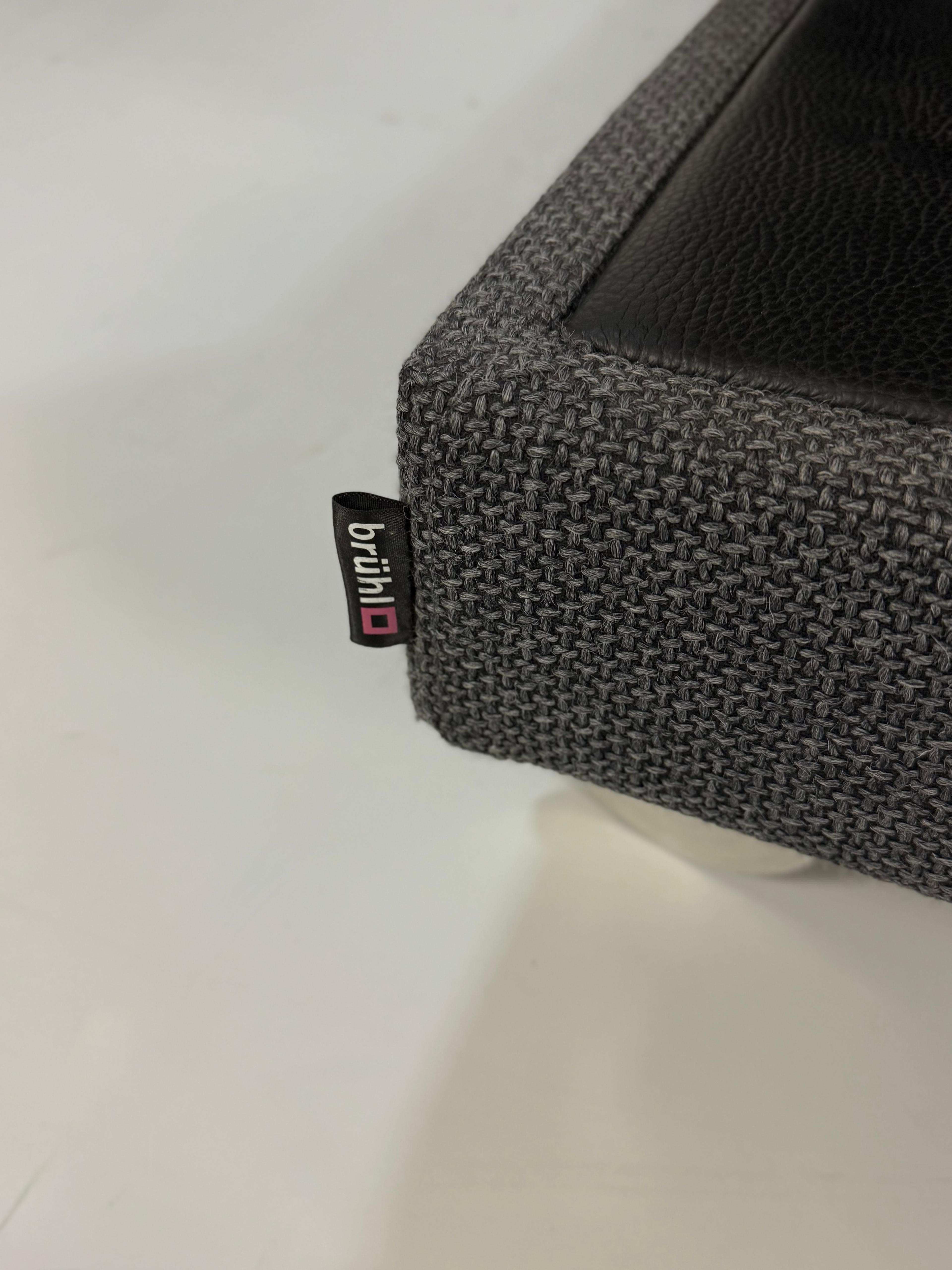 Ausstellungsstück Brühl Fourtwo Grau  Designer Stoff Sofa vor einer Wand, stilvoll und modern eingerichtet.