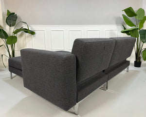 Ausstellungsstück Brühl Fourtwo Grau  Designer Stoff Sofa vor einer Wand, stilvoll und modern eingerichtet.