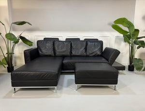 Brühl FourTwo Modell in der Farbe Schwarz Designer Leder Sofa vor einer Wand, stilvoll und modern eingerichtet.