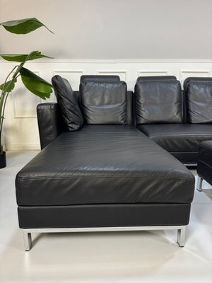 Brühl FourTwo Modell in der Farbe Schwarz Designer Leder Sofa vor einer Wand, stilvoll und modern eingerichtet.