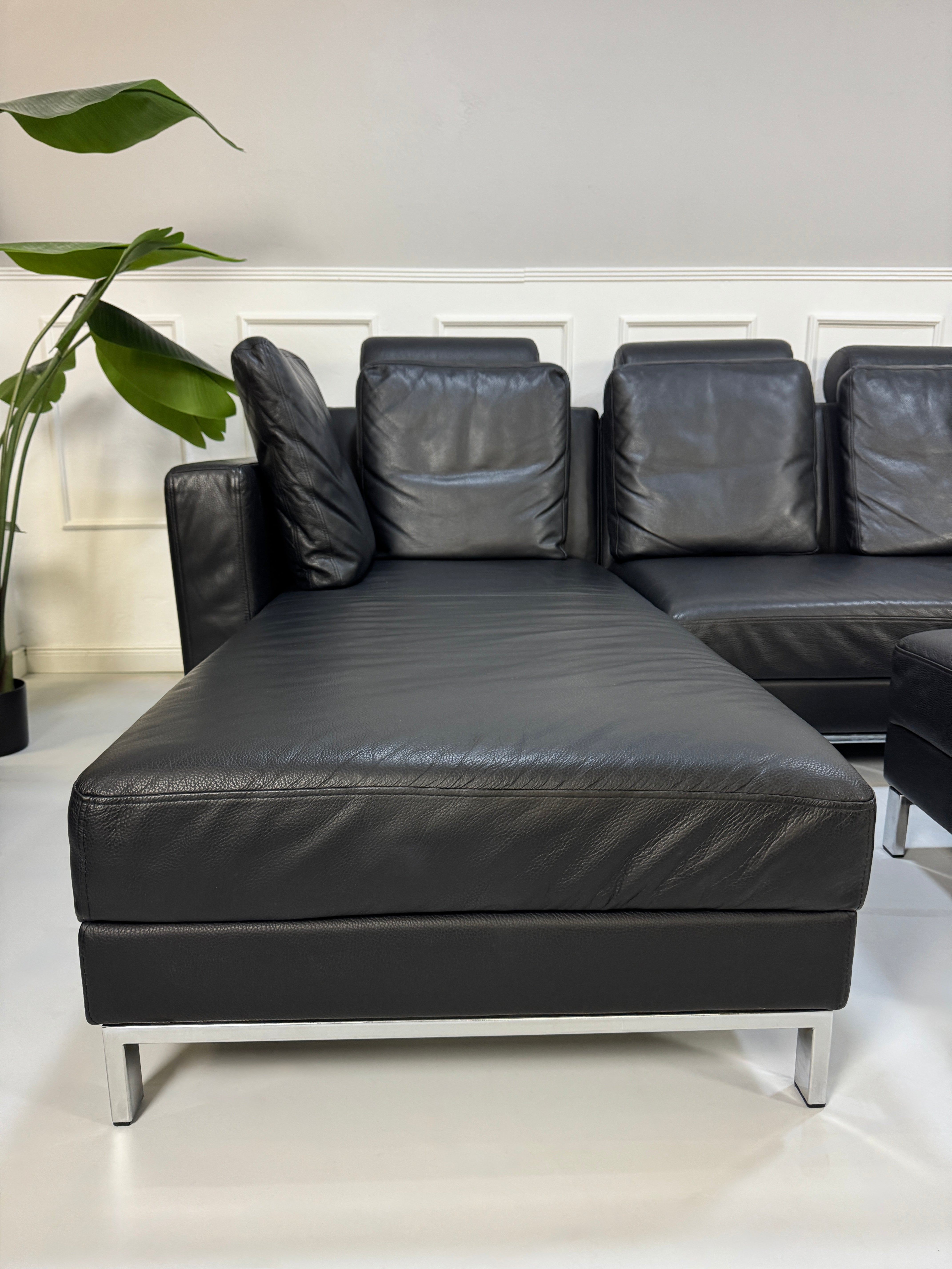 Brühl FourTwo Modell in der Farbe Schwarz Designer Leder Sofa vor einer Wand, stilvoll und modern eingerichtet.
