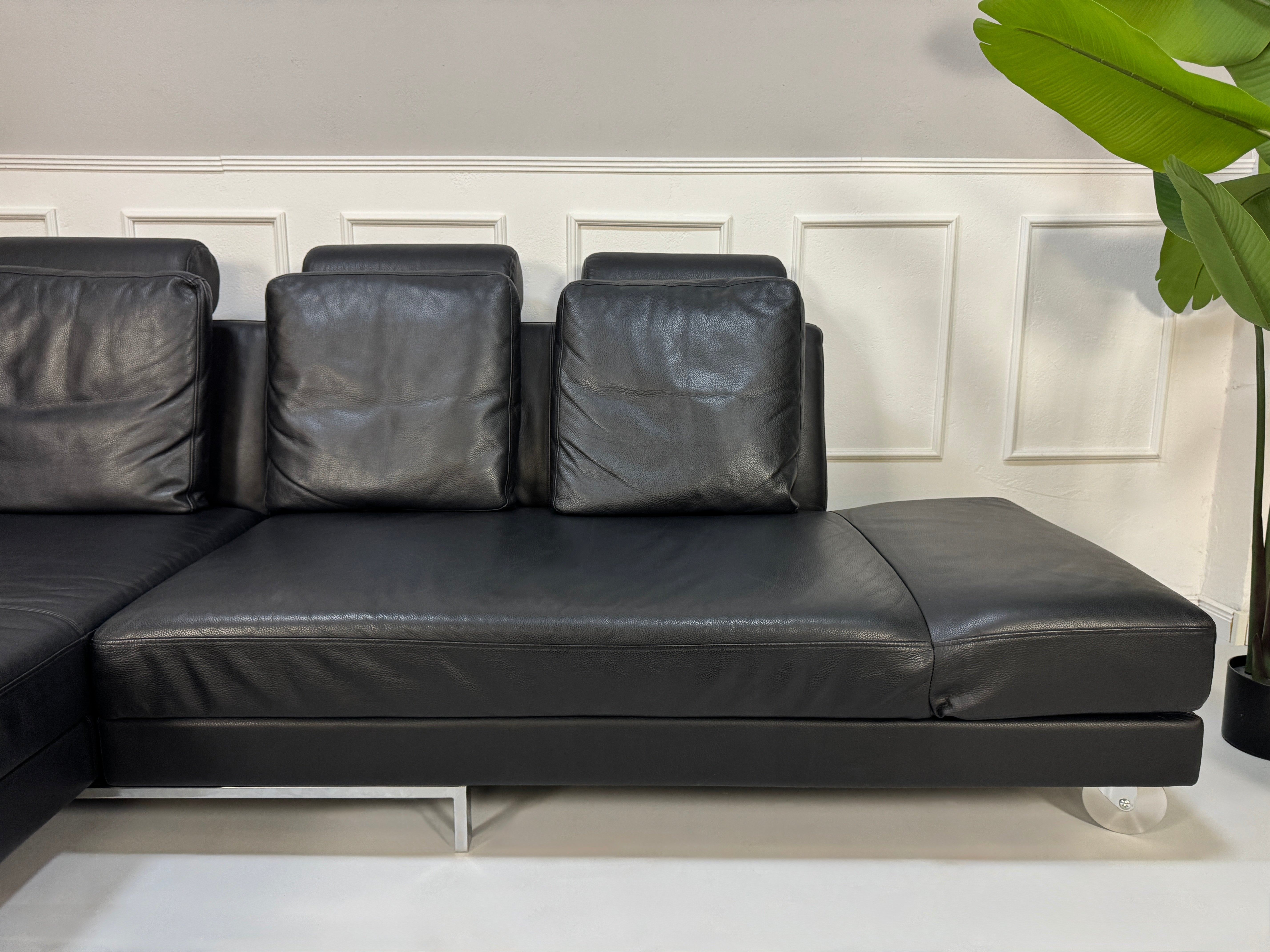 Brühl FourTwo Modell in der Farbe Schwarz Designer Leder Sofa vor einer Wand, stilvoll und modern eingerichtet.