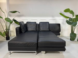 Brühl FourTwo Modell in der Farbe Schwarz Designer Leder Sofa vor einer Wand, stilvoll und modern eingerichtet.