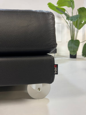 Brühl FourTwo Modell in der Farbe Schwarz Designer Leder Sofa vor einer Wand, stilvoll und modern eingerichtet.