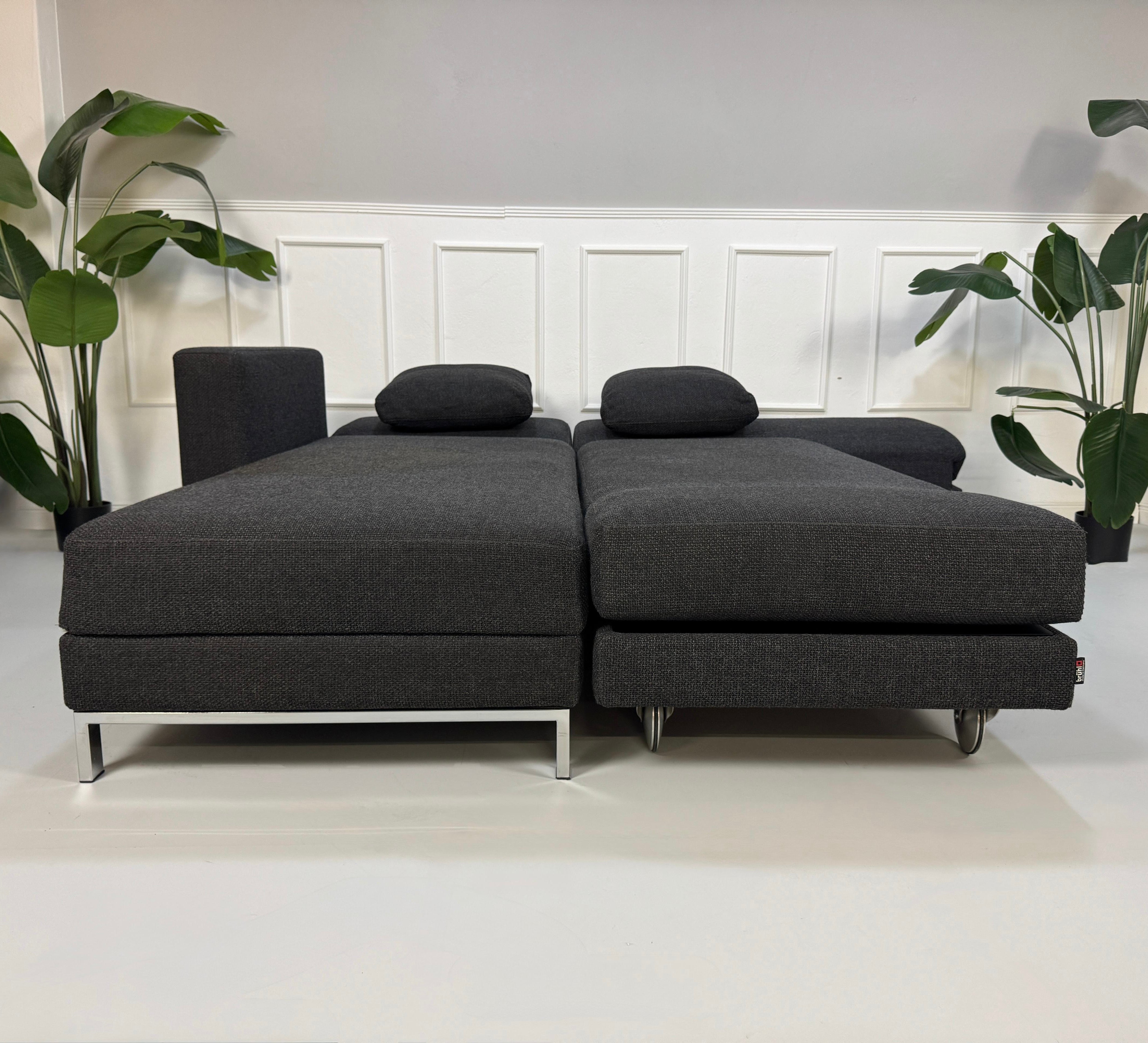 Gebrauchtes graues Brühl Fourtwo Designer Stoff Sofa vor einer Wand, stilvoll und modern eingerichtet.