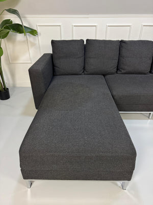 Gebrauchtes graues Brühl Fourtwo Designer Stoff Sofa vor einer Wand, stilvoll und modern eingerichtet.