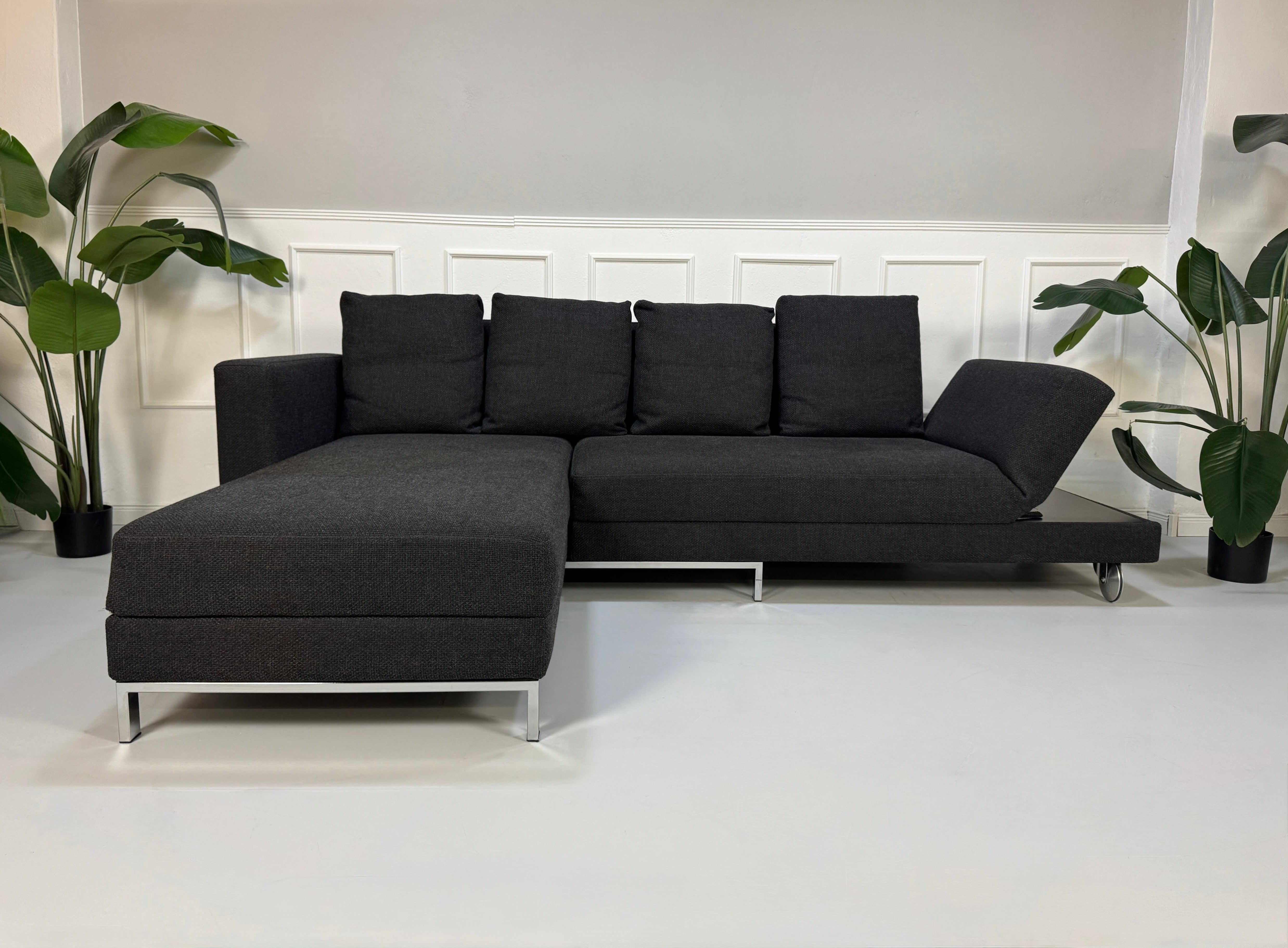 Gebrauchtes graues Brühl Fourtwo Designer Stoff Sofa vor einer Wand, stilvoll und modern eingerichtet.