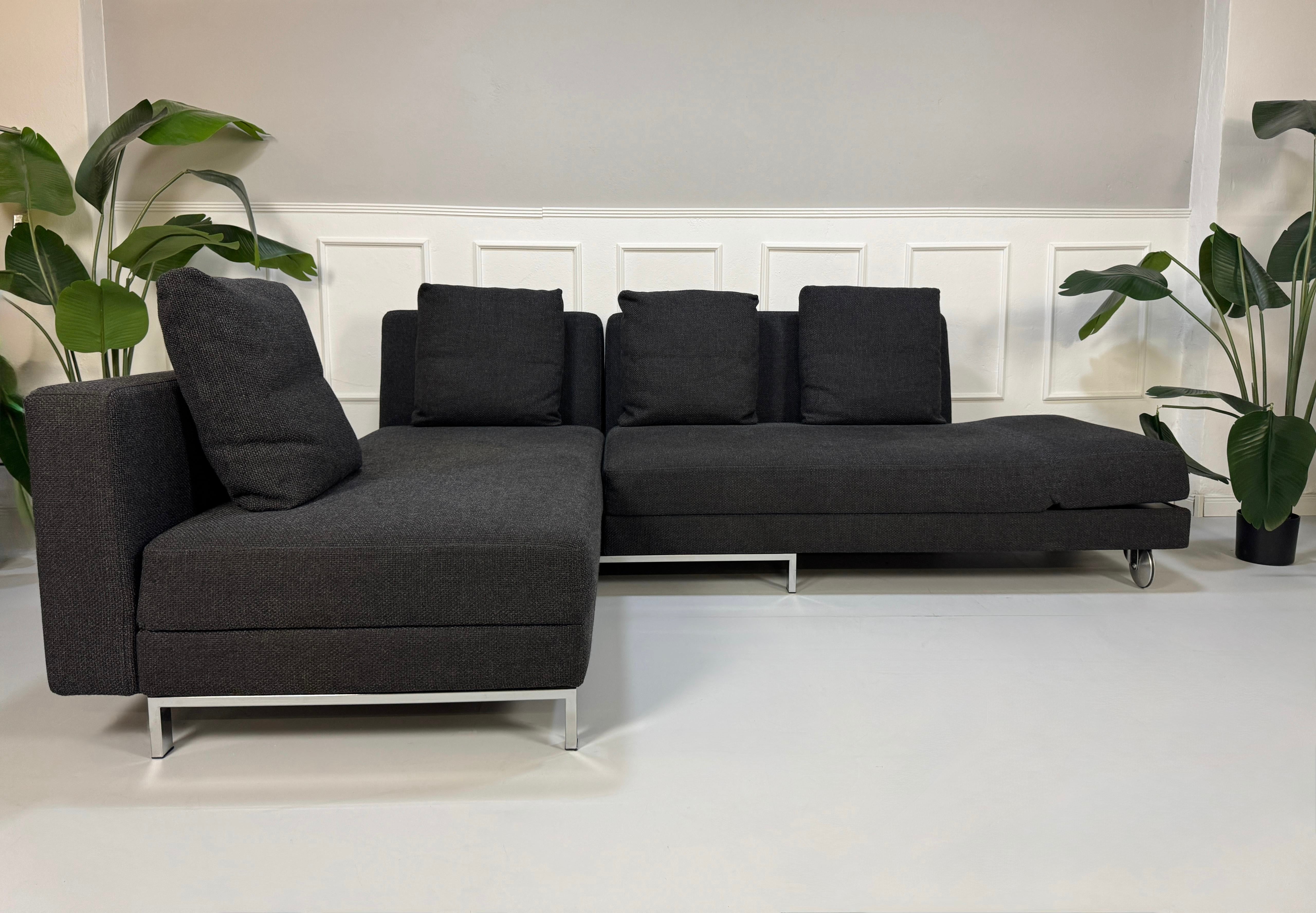 Gebrauchtes graues Brühl Fourtwo Designer Stoff Sofa vor einer Wand, stilvoll und modern eingerichtet.