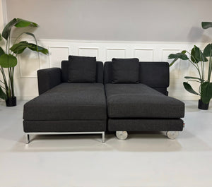 Gebrauchtes graues Brühl Fourtwo Designer Stoff Sofa vor einer Wand, stilvoll und modern eingerichtet.