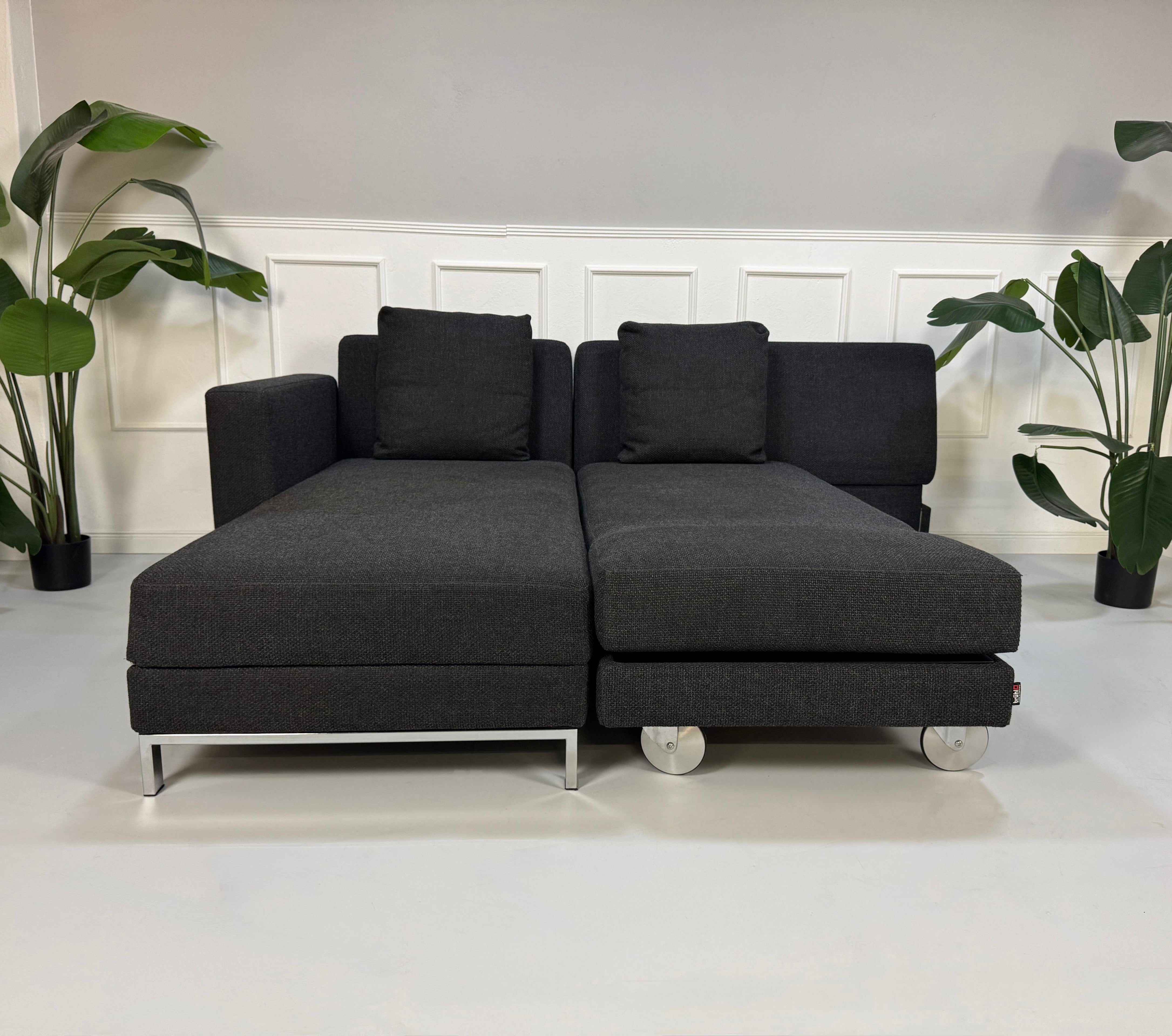 Gebrauchtes graues Brühl Fourtwo Designer Stoff Sofa vor einer Wand, stilvoll und modern eingerichtet.