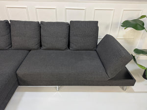 Gebrauchtes graues Brühl Fourtwo Designer Stoff Sofa vor einer Wand, stilvoll und modern eingerichtet.