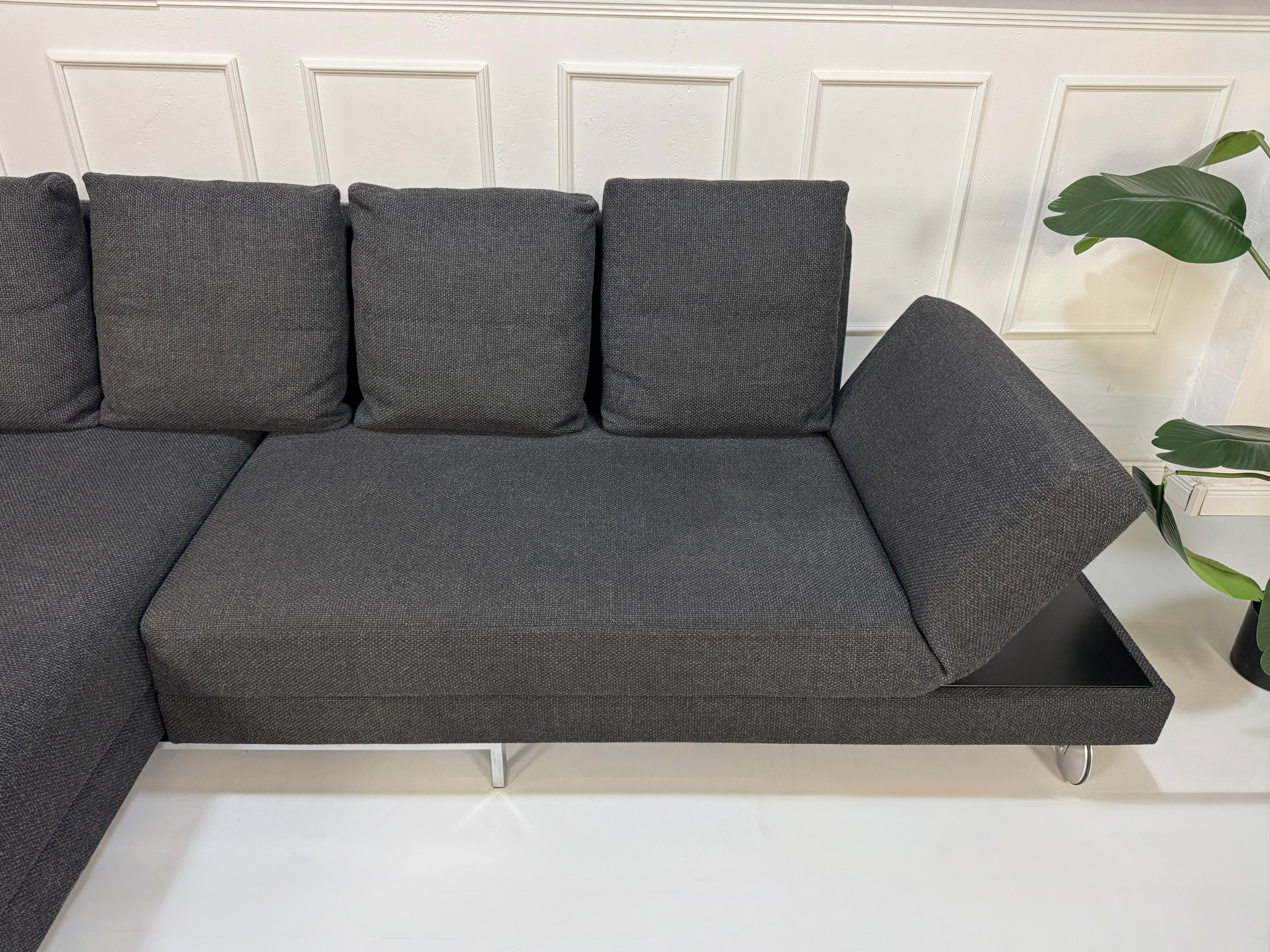 Gebrauchtes graues Brühl Fourtwo Designer Stoff Sofa vor einer Wand, stilvoll und modern eingerichtet.