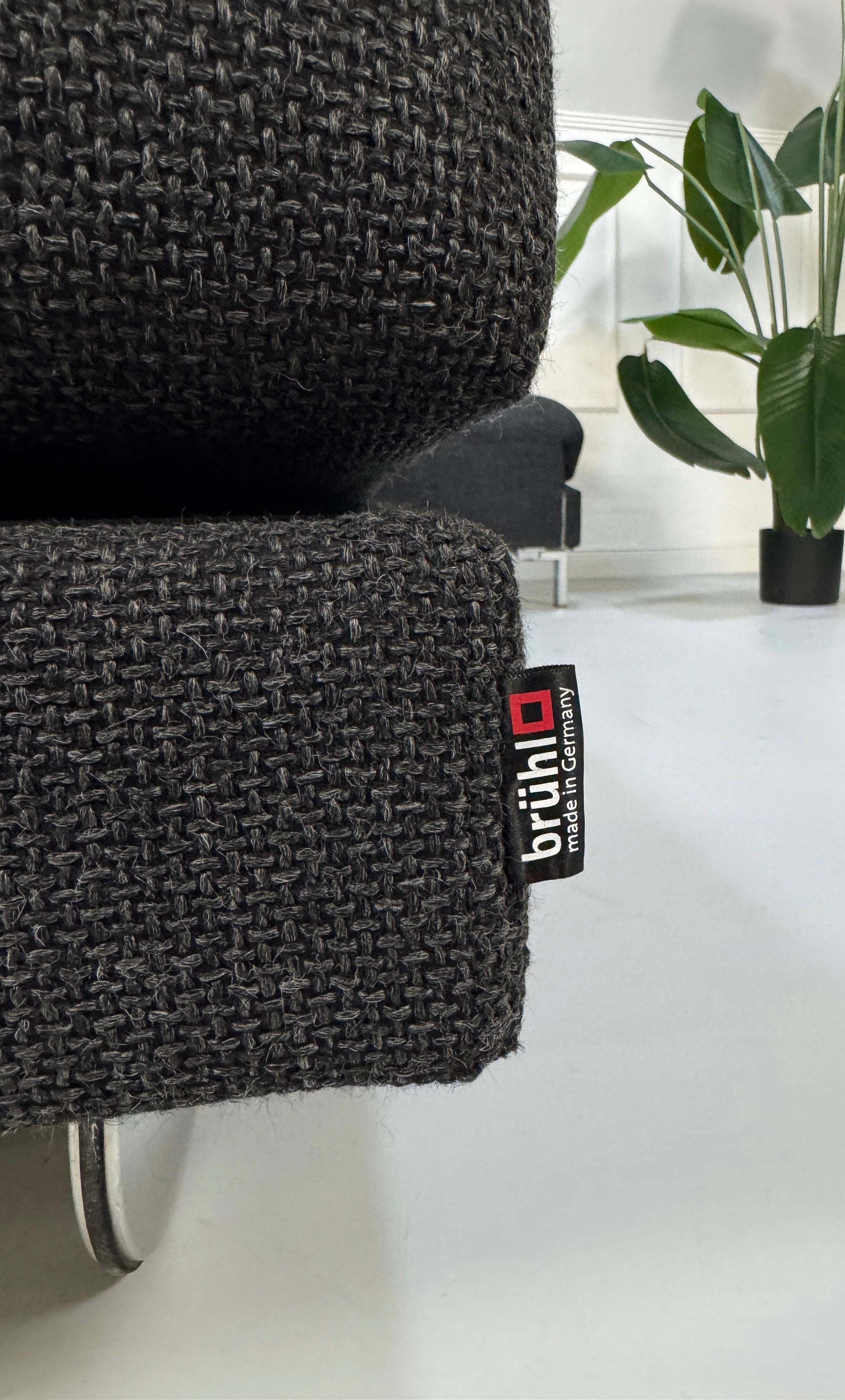 Gebrauchtes graues Brühl Fourtwo Designer Stoff Sofa vor einer Wand, stilvoll und modern eingerichtet.
