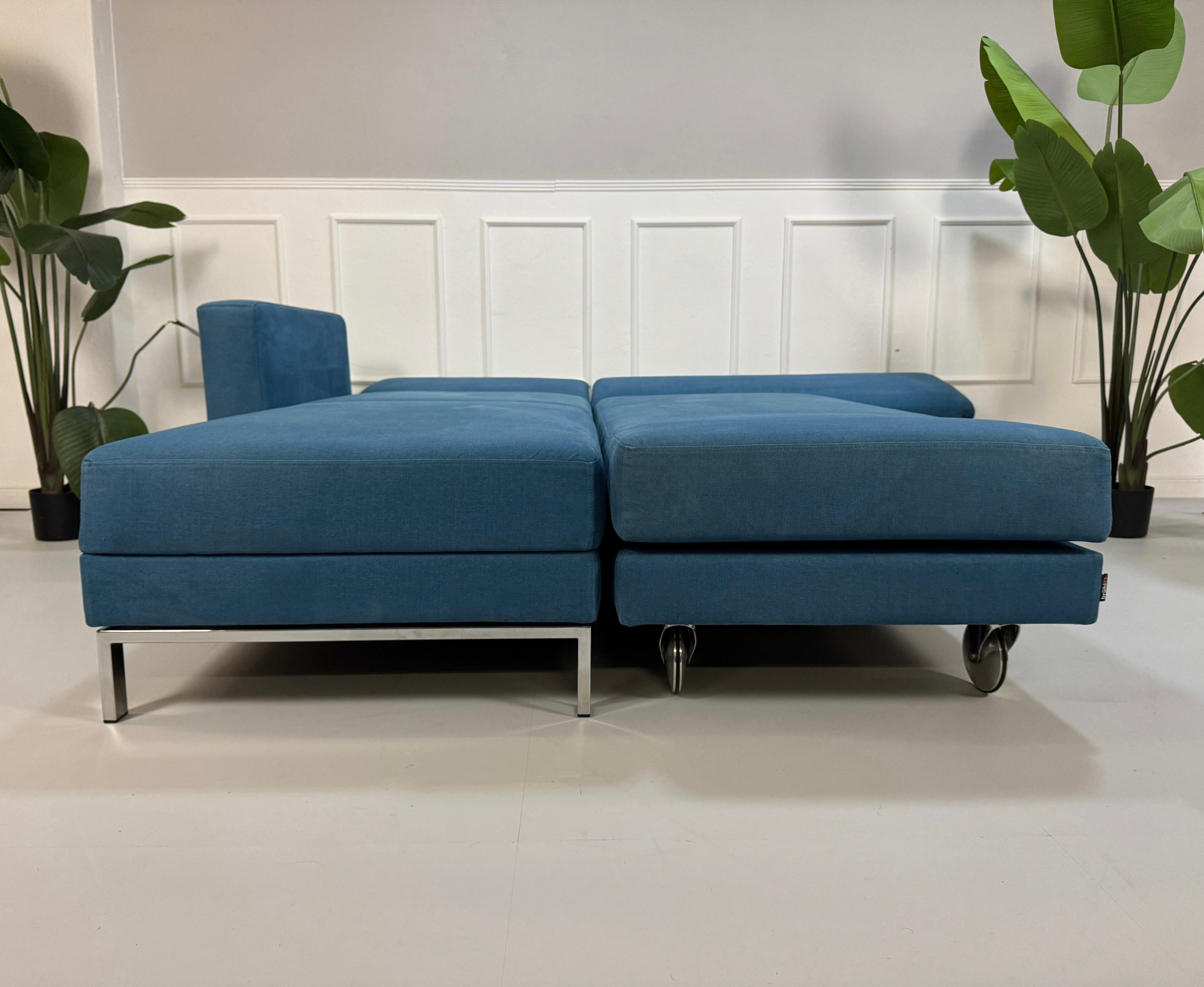 Gebrauchtes blaues Brühl Fourtwo Designer Stoff Sofa vor einer Wand, stilvoll und modern eingerichtet.