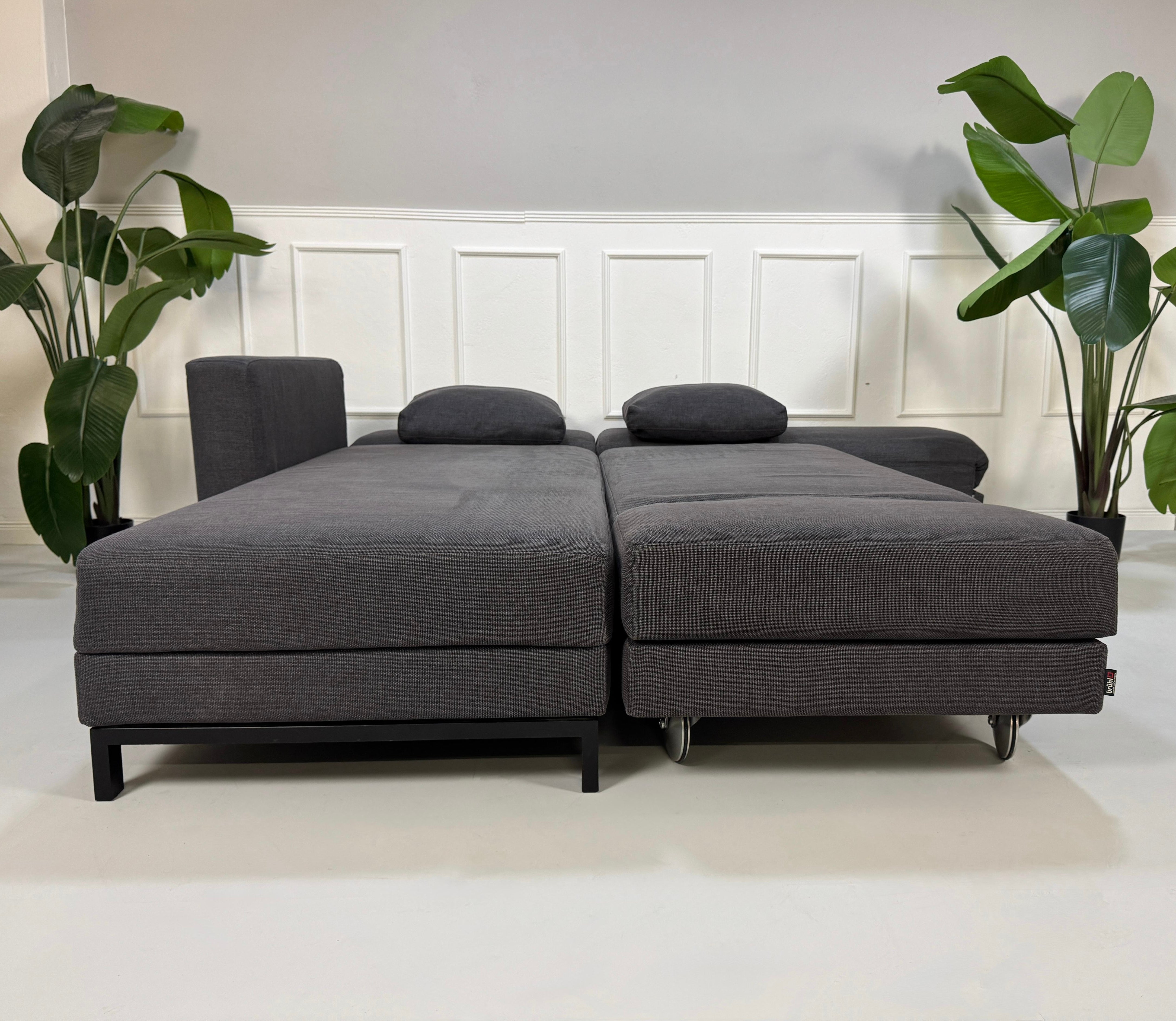 Erneuertes Brühl Fourtwo in Grau Designer Stoff Sofa vor einer Wand, stilvoll und modern eingerichtet.