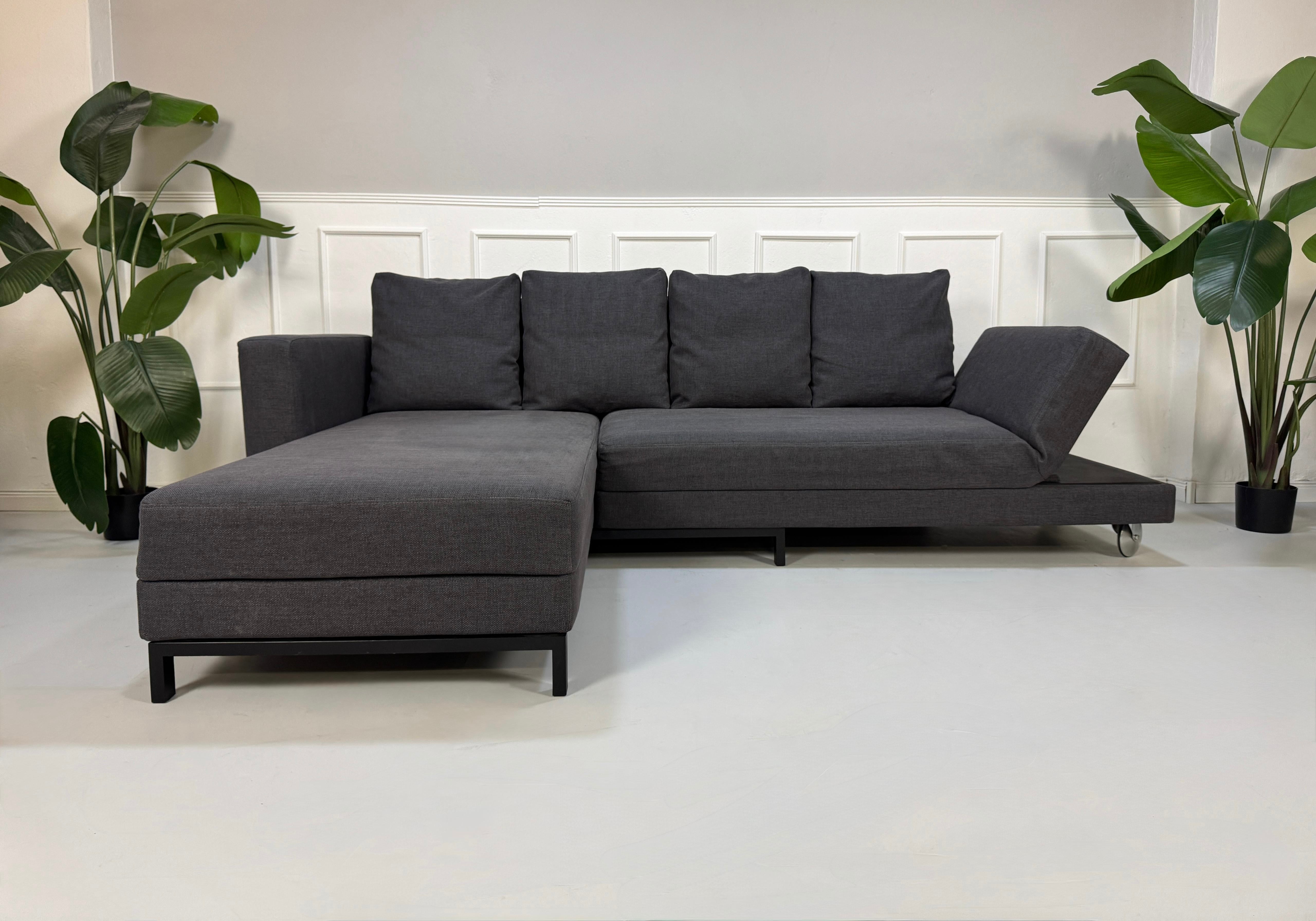 Erneuertes Brühl Fourtwo in Grau Designer Stoff Sofa vor einer Wand, stilvoll und modern eingerichtet.