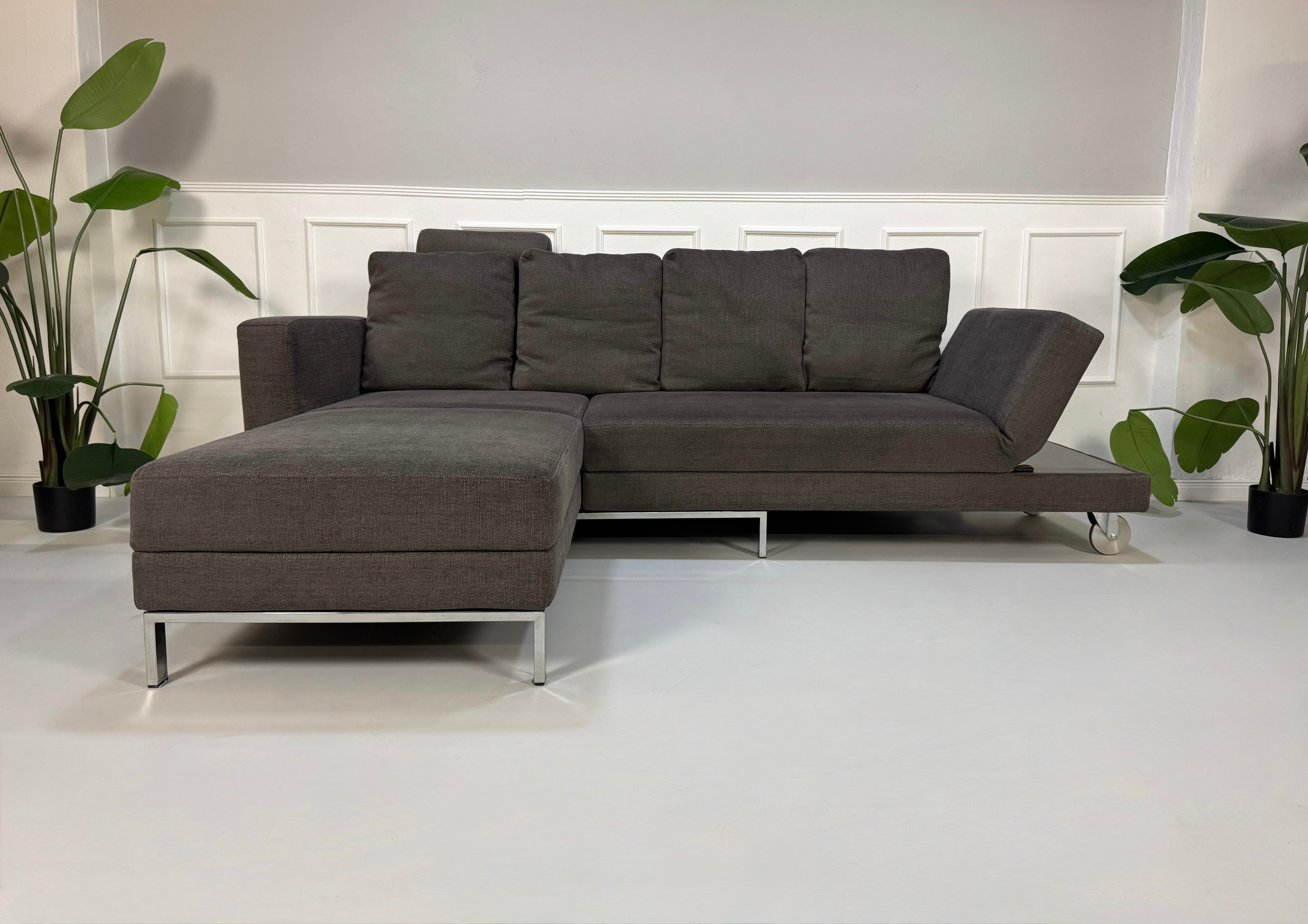 Gebrauchtes grau braunes Brühl Fourtwo Designer Stoff Sofa vor einer Wand, stilvoll und modern eingerichtet.