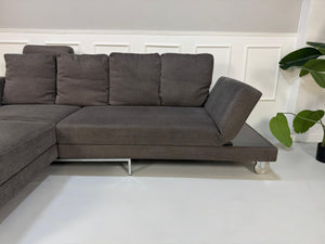 Gebrauchtes grau braunes Brühl Fourtwo Designer Stoff Sofa vor einer Wand, stilvoll und modern eingerichtet.