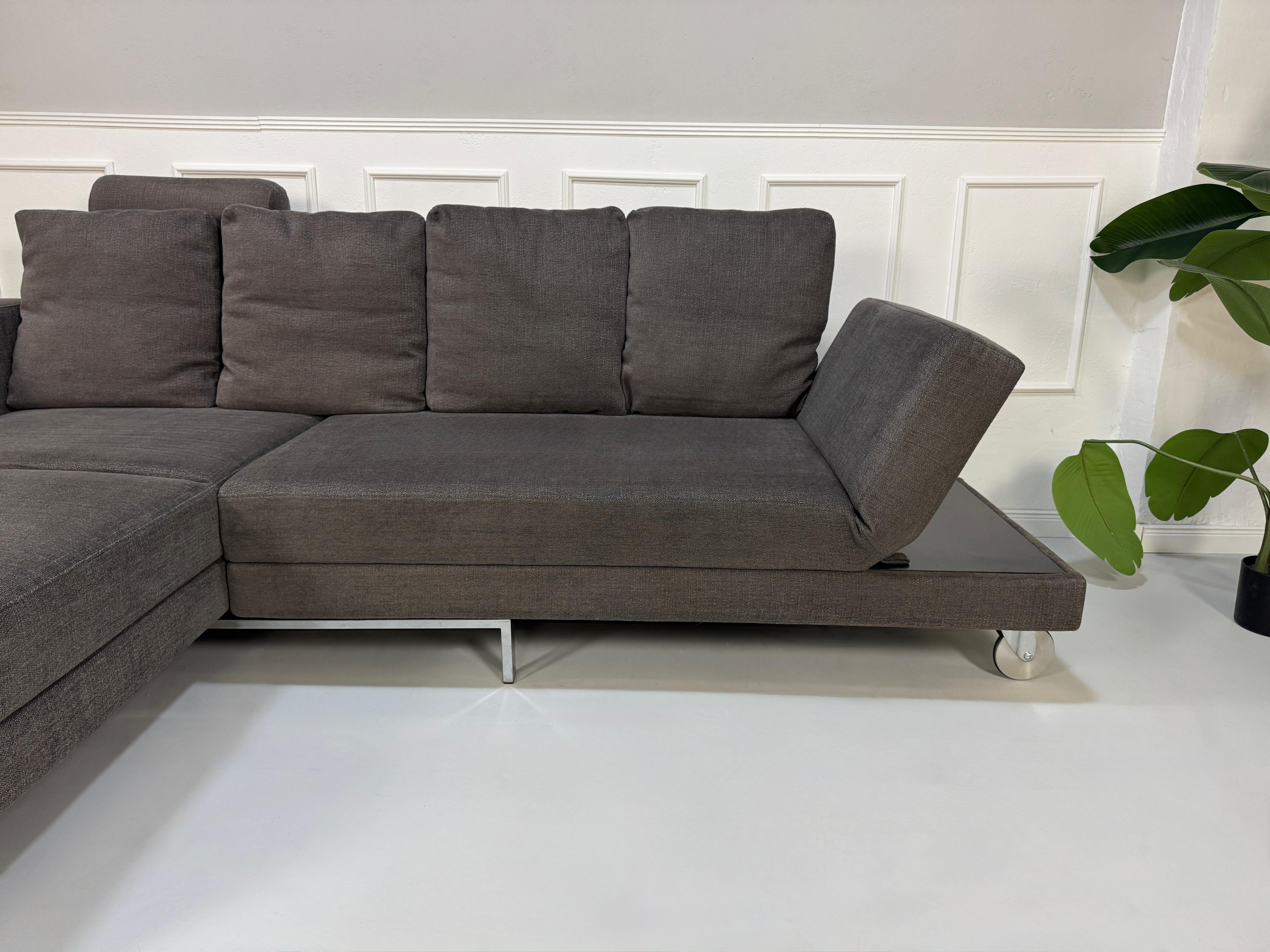 Gebrauchtes grau braunes Brühl Fourtwo Designer Stoff Sofa vor einer Wand, stilvoll und modern eingerichtet.