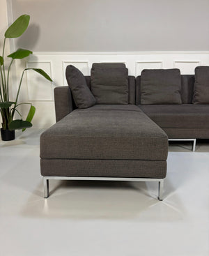Gebrauchtes grau braunes Brühl Fourtwo Designer Stoff Sofa vor einer Wand, stilvoll und modern eingerichtet.