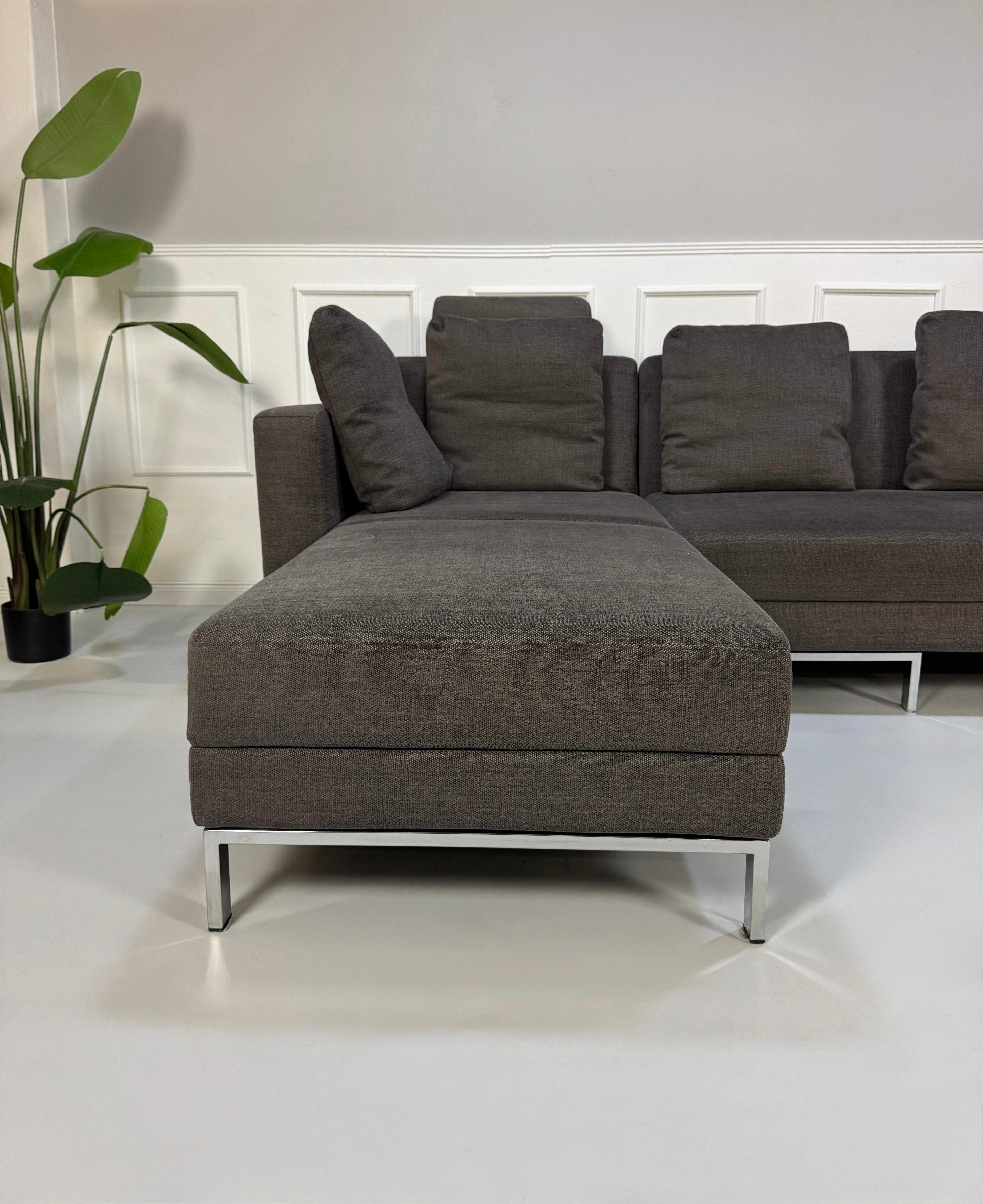 Gebrauchtes grau braunes Brühl Fourtwo Designer Stoff Sofa vor einer Wand, stilvoll und modern eingerichtet.
