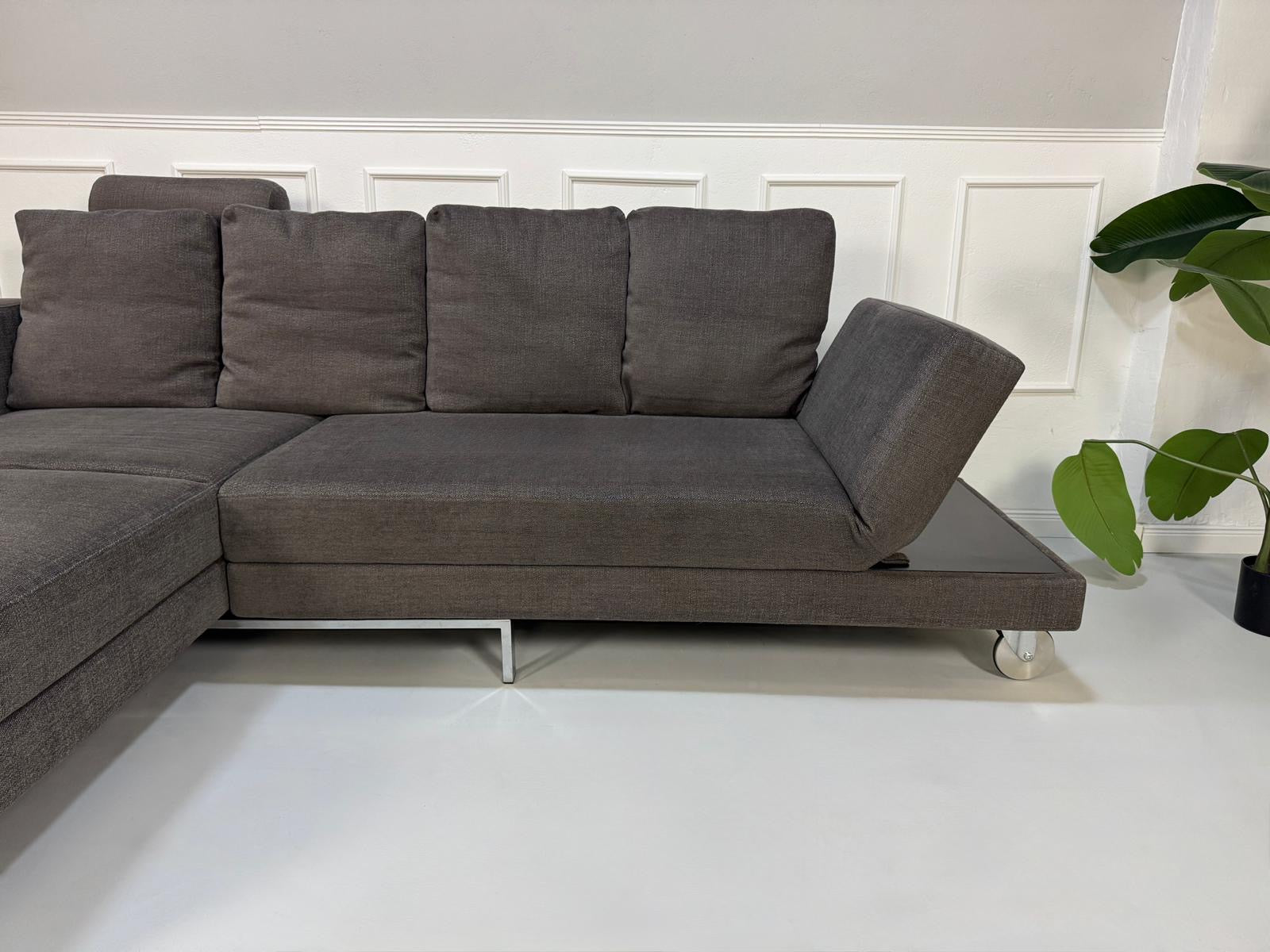 Gebrauchtes grau braunes Brühl Fourtwo Designer Stoff Sofa vor einer Wand, stilvoll und modern eingerichtet.