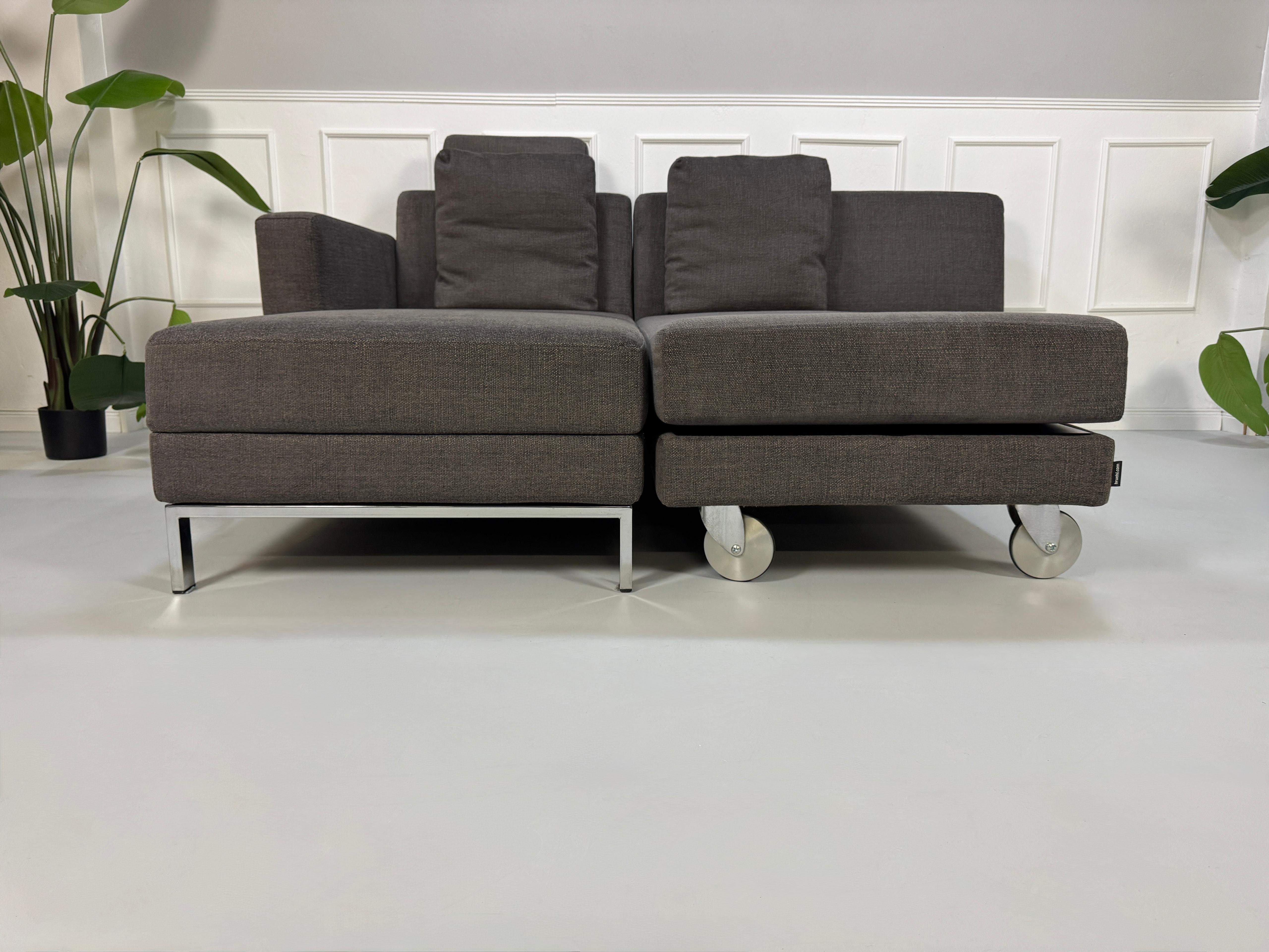 Gebrauchtes grau braunes Brühl Fourtwo Designer Stoff Sofa vor einer Wand, stilvoll und modern eingerichtet.