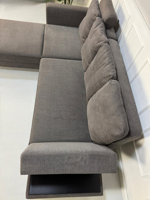 Gebrauchtes grau braunes Brühl Fourtwo Designer Stoff Sofa vor einer Wand, stilvoll und modern eingerichtet.