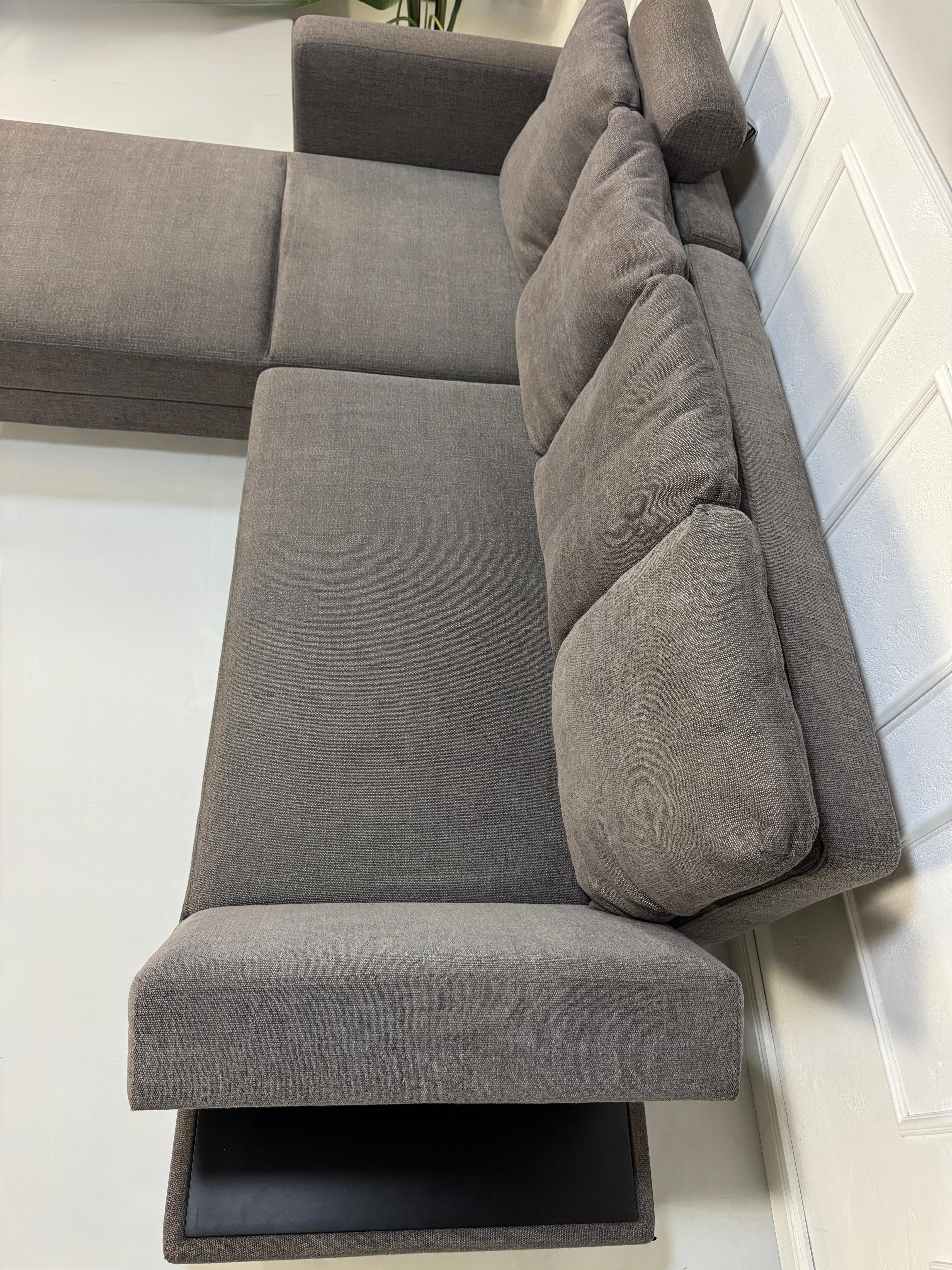 Gebrauchtes grau braunes Brühl Fourtwo Designer Stoff Sofa vor einer Wand, stilvoll und modern eingerichtet.