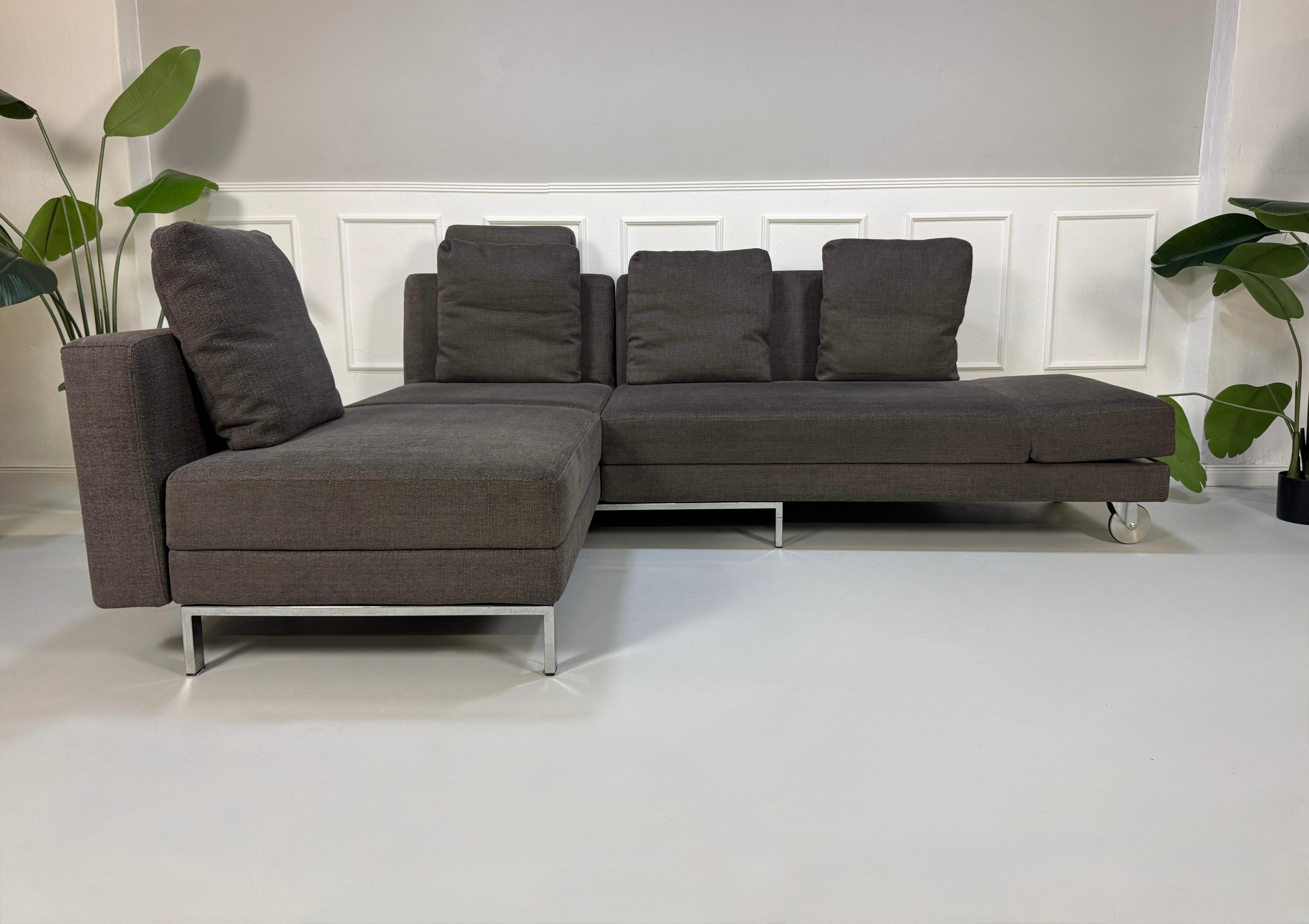 Gebrauchtes grau braunes Brühl Fourtwo Designer Stoff Sofa vor einer Wand, stilvoll und modern eingerichtet.