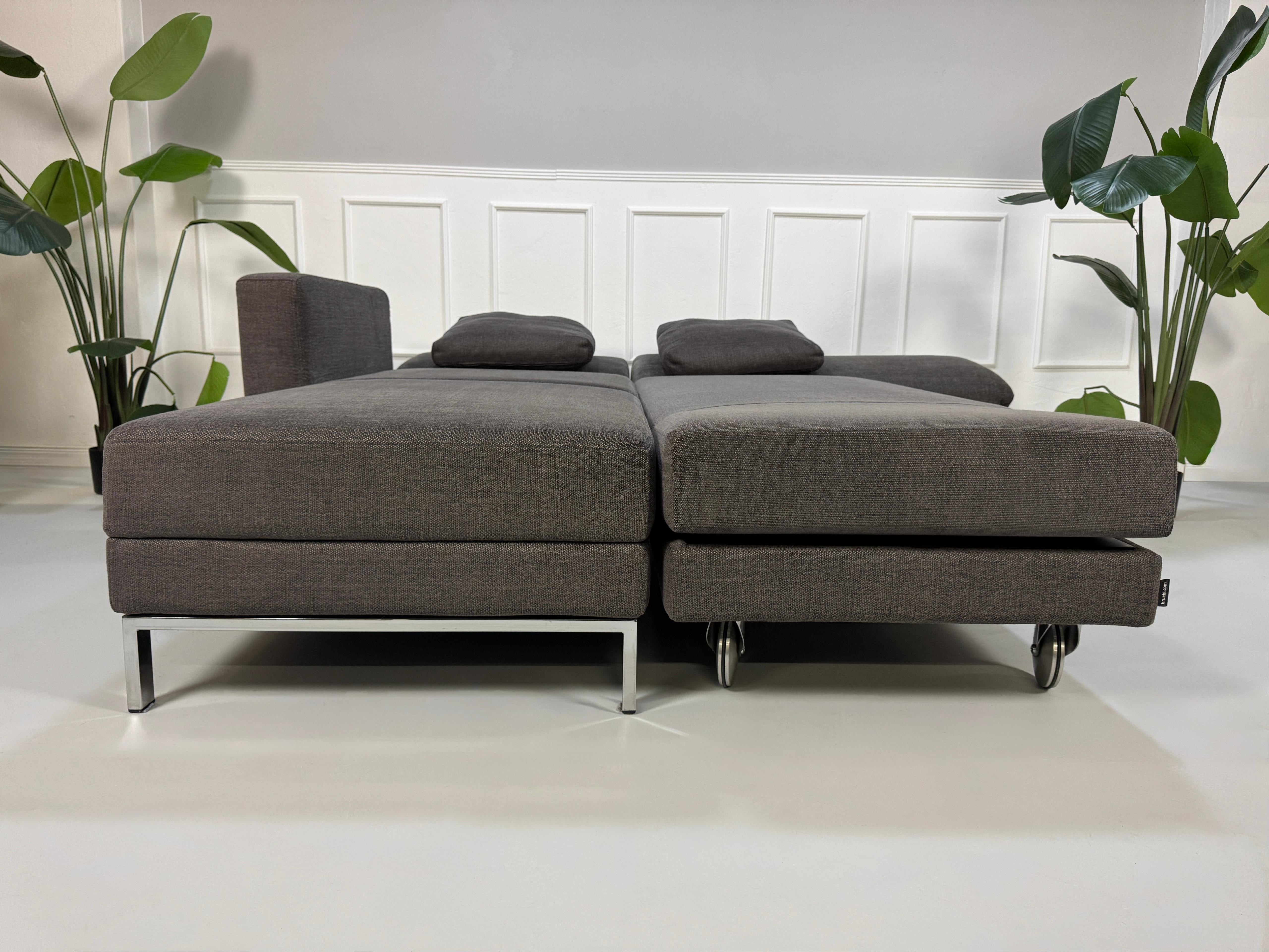 Gebrauchtes grau braunes Brühl Fourtwo Designer Stoff Sofa vor einer Wand, stilvoll und modern eingerichtet.