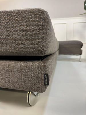 Gebrauchtes grau braunes Brühl Fourtwo Designer Stoff Sofa vor einer Wand, stilvoll und modern eingerichtet.