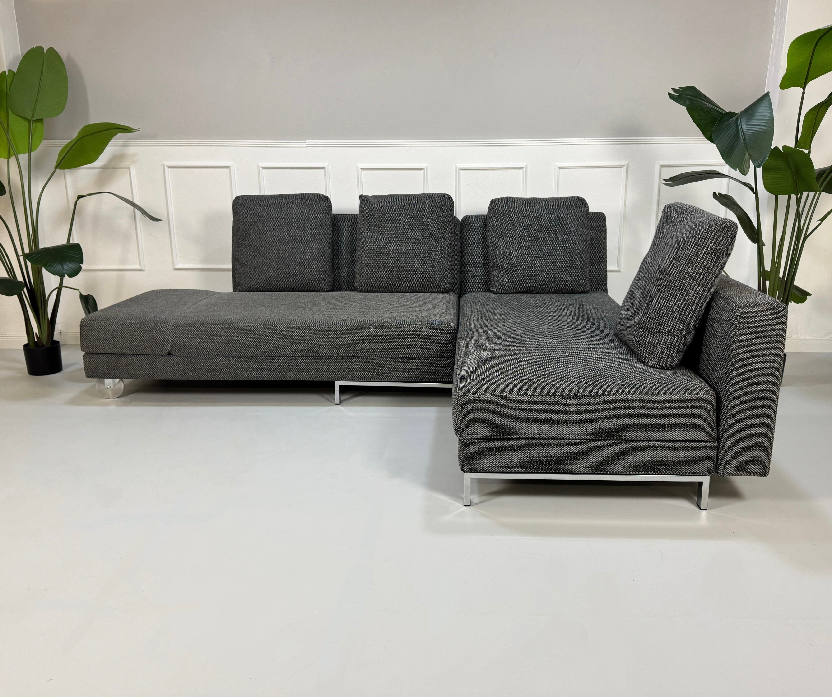 Gebrauchtes graues Brühl Fourtwo Designer Stoff Sofa mit Kissen vor einer Wand, stilvoll und modern eingerichtet.