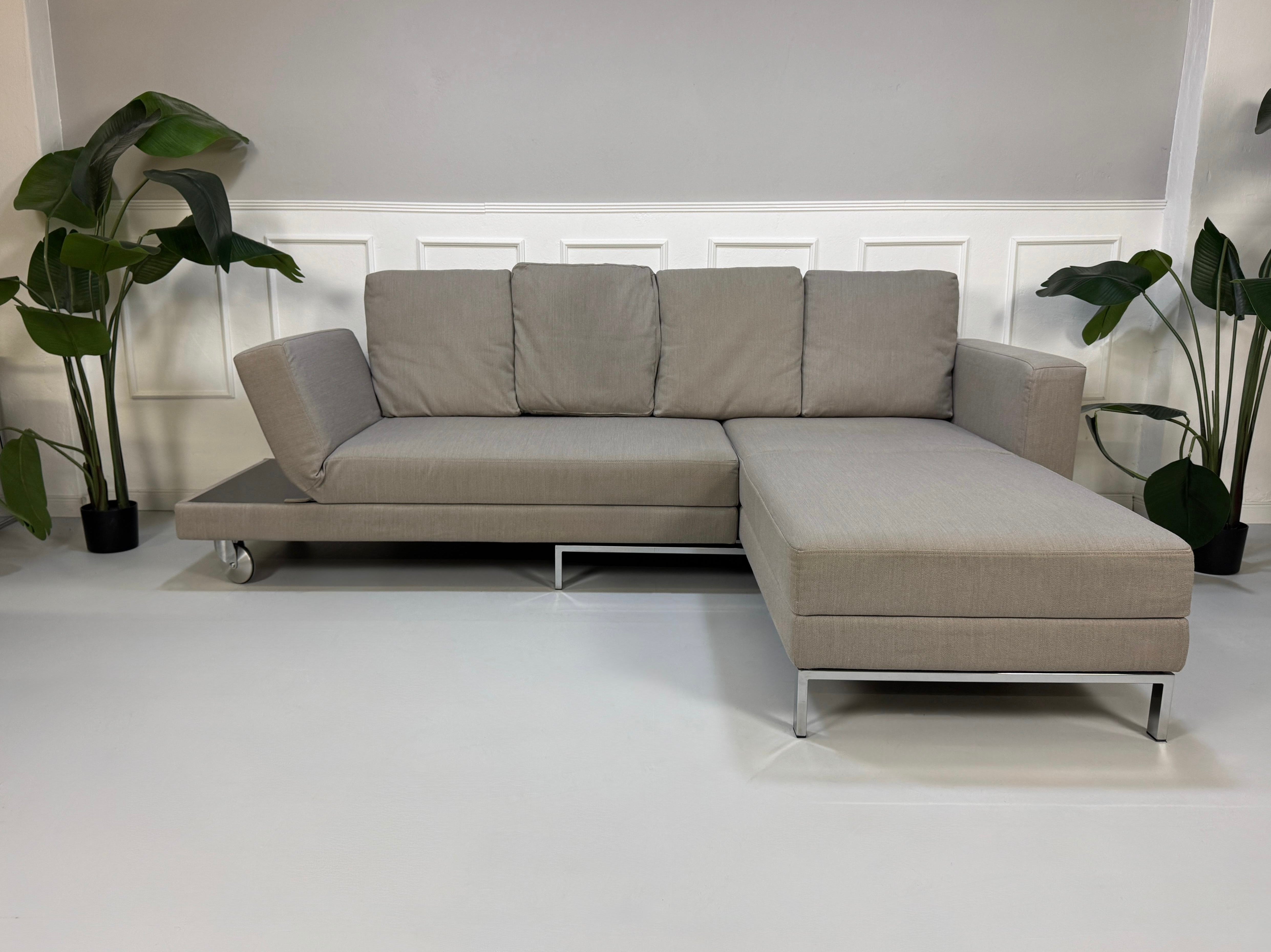 Gebrauchtes graues Brühl Fourtwo Designer Stoff Sofa vor einer Wand, stilvoll und modern eingerichtet.
