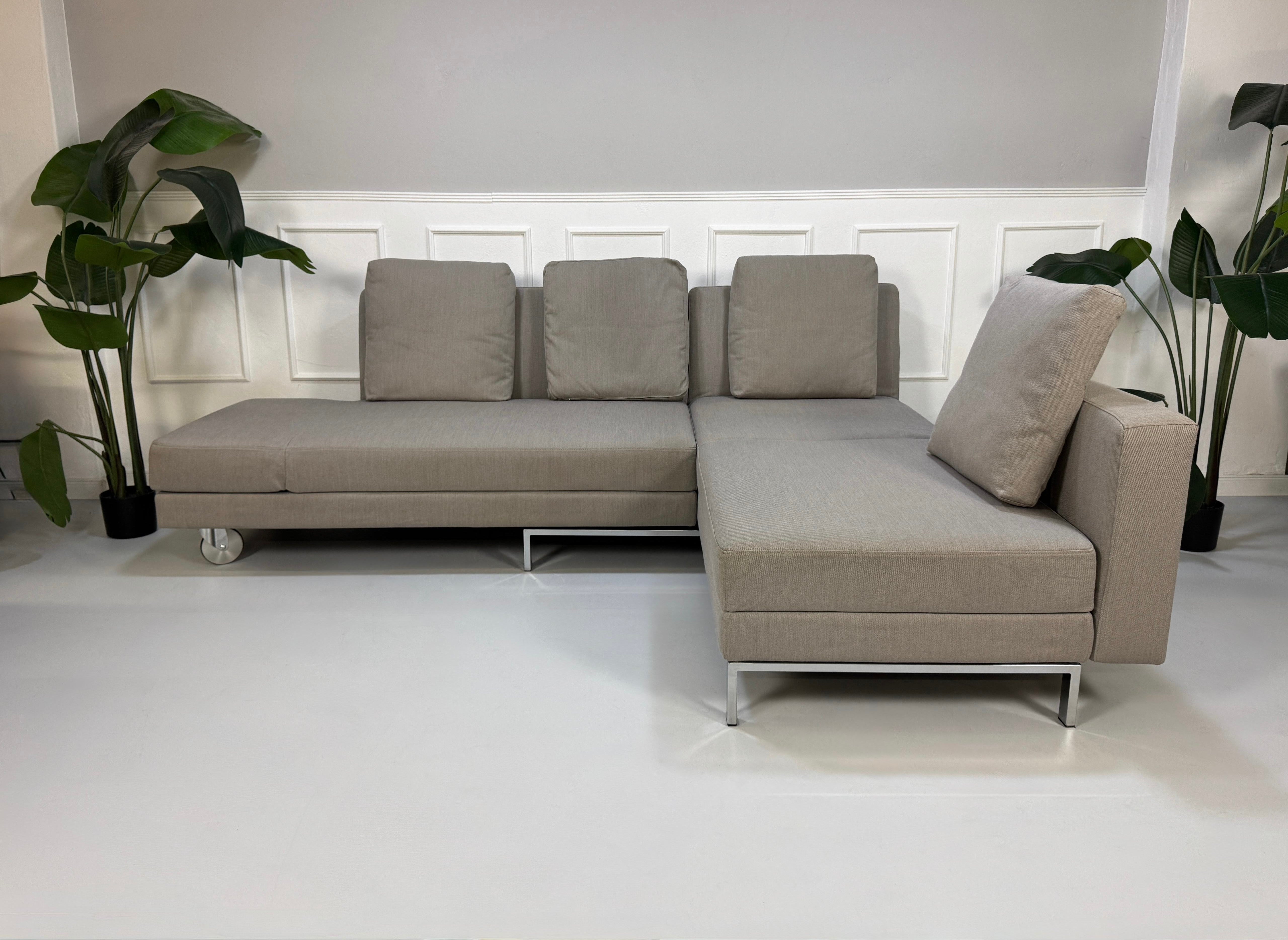 Gebrauchtes graues Brühl Fourtwo Designer Stoff Sofa vor einer Wand, stilvoll und modern eingerichtet.