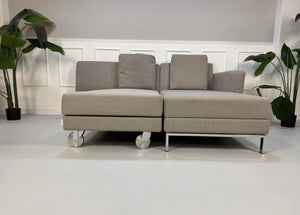 Gebrauchtes graues Brühl Fourtwo Designer Stoff Sofa vor einer Wand, stilvoll und modern eingerichtet.