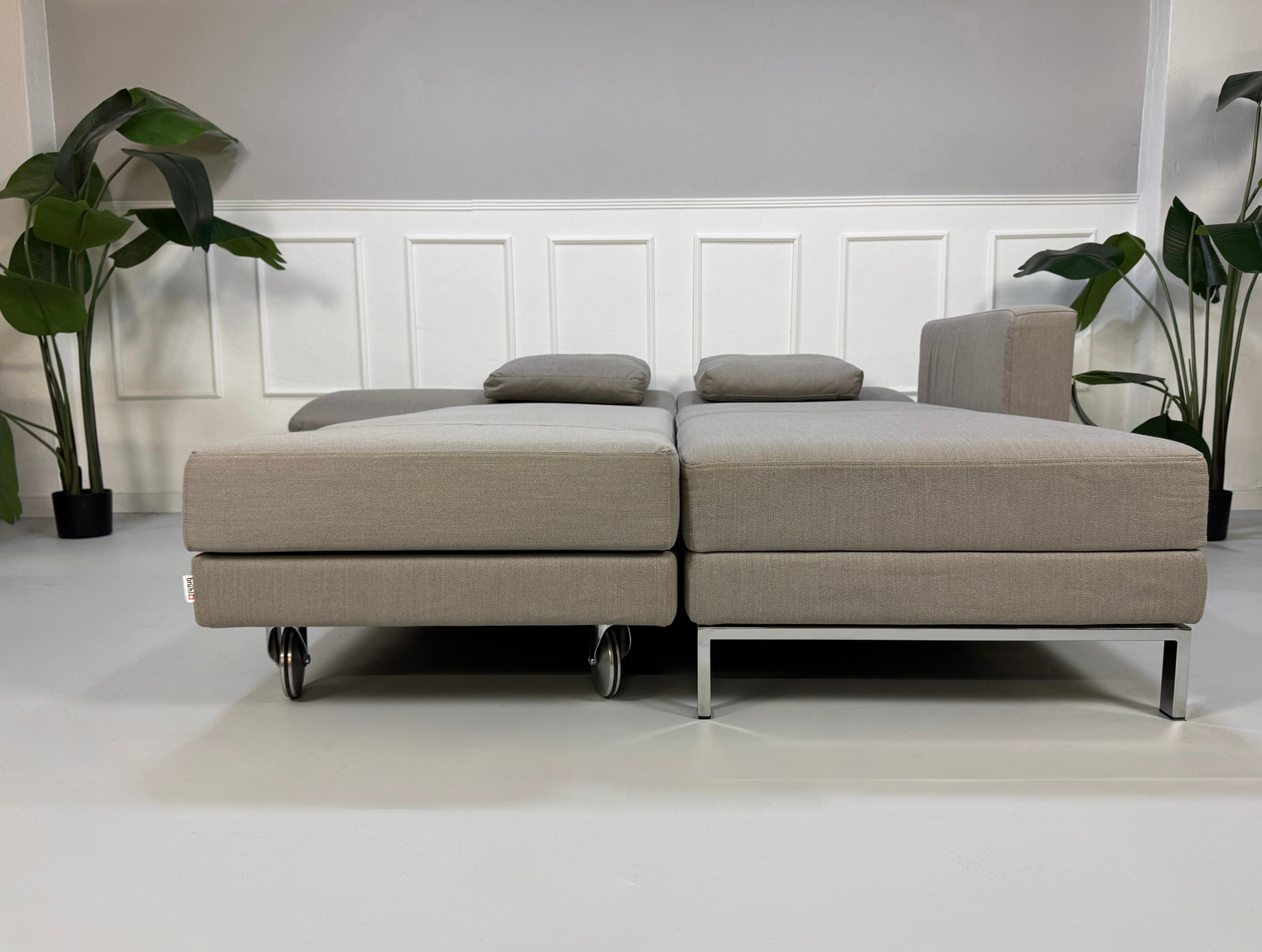Gebrauchtes graues Brühl Fourtwo Designer Stoff Sofa vor einer Wand, stilvoll und modern eingerichtet.