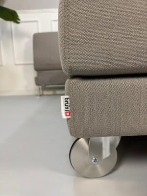 Gebrauchtes graues Brühl Fourtwo Designer Stoff Sofa vor einer Wand, stilvoll und modern eingerichtet.