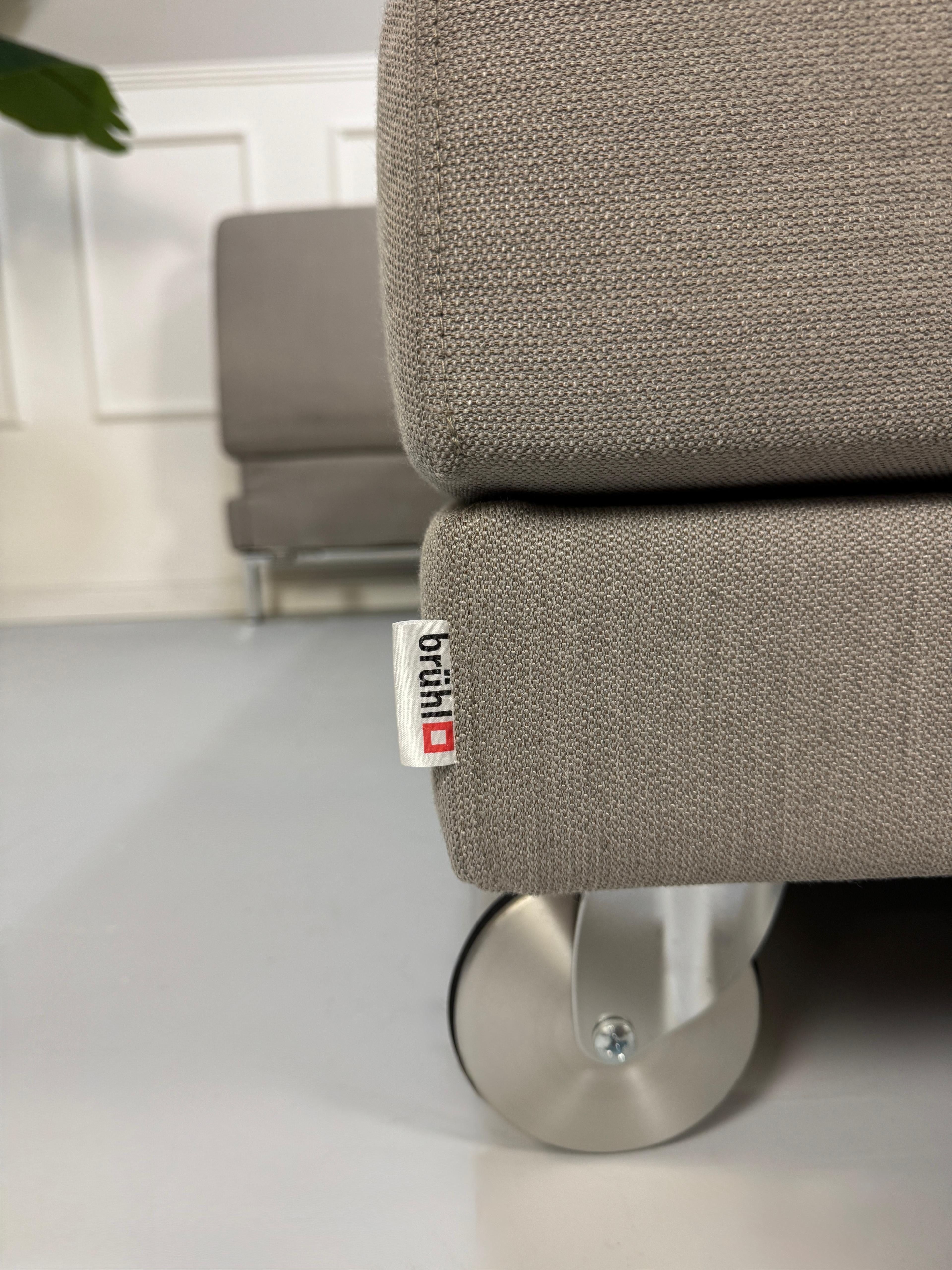 Gebrauchtes graues Brühl Fourtwo Designer Stoff Sofa vor einer Wand, stilvoll und modern eingerichtet.
