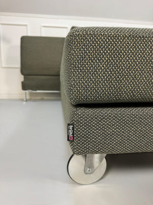 Grau Grünes Brühl Fourtwo Designer Stoff Sofa vor einer Wand, stilvoll und modern eingerichtet.