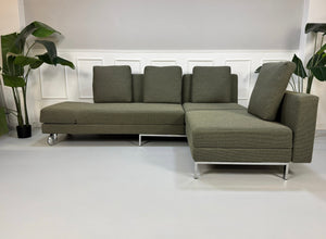 Grau Grünes Brühl Fourtwo Designer Stoff Sofa vor einer Wand, stilvoll und modern eingerichtet.