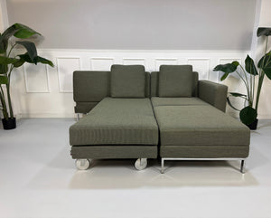 Grau Grünes Brühl Fourtwo Designer Stoff Sofa vor einer Wand, stilvoll und modern eingerichtet.