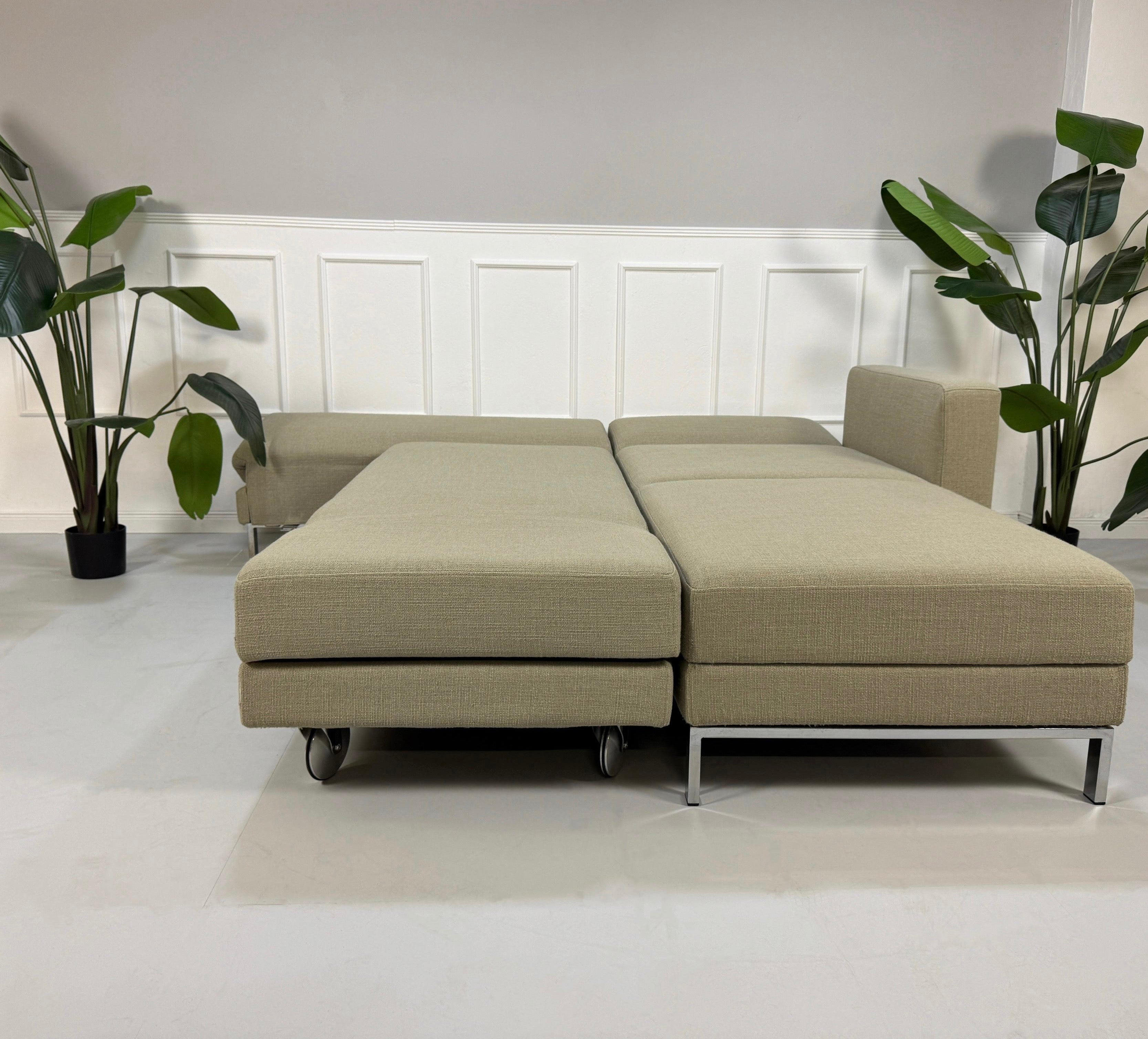 Gebrauchtes graues Brühl Fourtwo Designer Stoff Sofa vor einer Wand, stilvoll und modern eingerichtet.