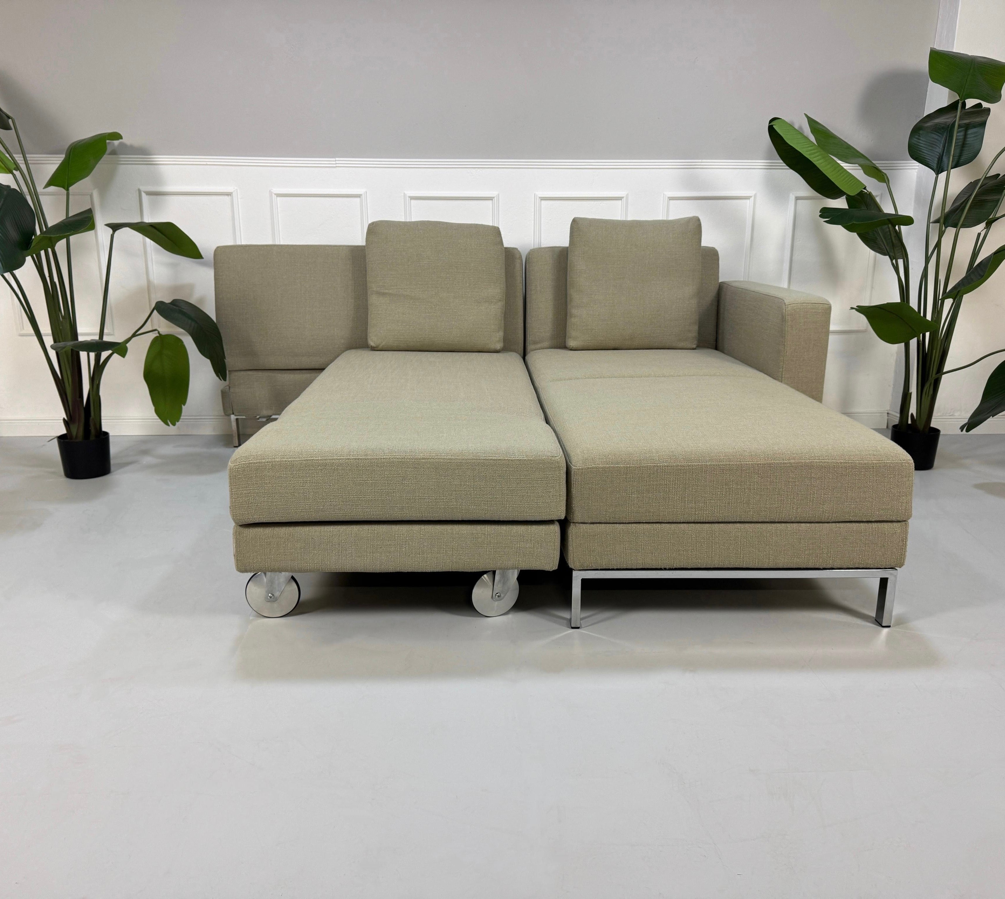 Gebrauchtes graues Brühl Fourtwo Designer Stoff Sofa vor einer Wand, stilvoll und modern eingerichtet.