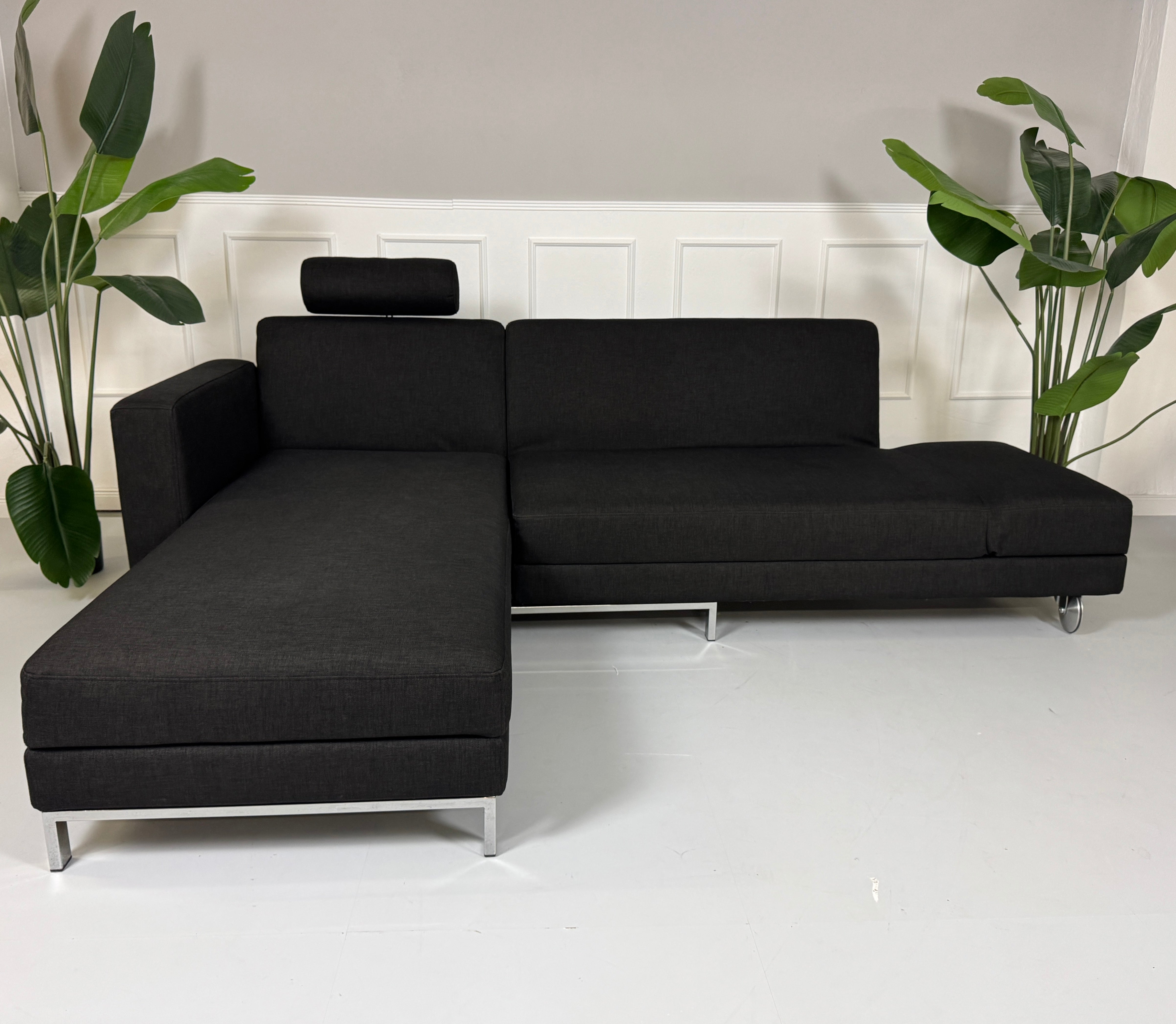 Erneuertes schwarzes Brühl Designer Stoff Sofa vor einer Wand, stilvoll und modern eingerichtet.