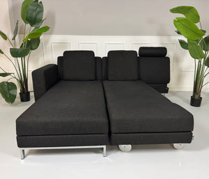 Erneuertes schwarzes Brühl Designer Stoff Sofa vor einer Wand, stilvoll und modern eingerichtet.