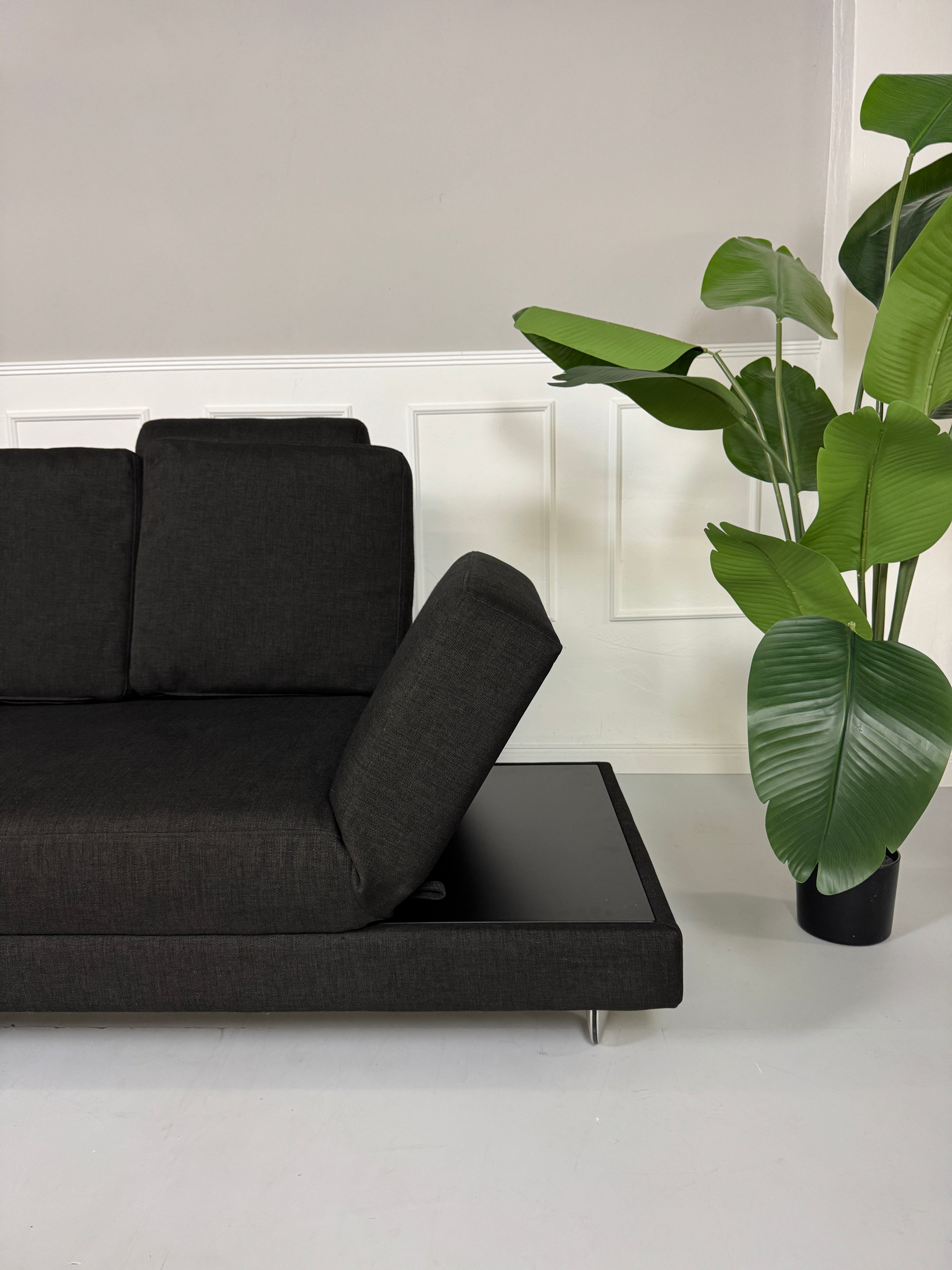 Erneuertes schwarzes Brühl Designer Stoff Sofa vor einer Wand, stilvoll und modern eingerichtet.
