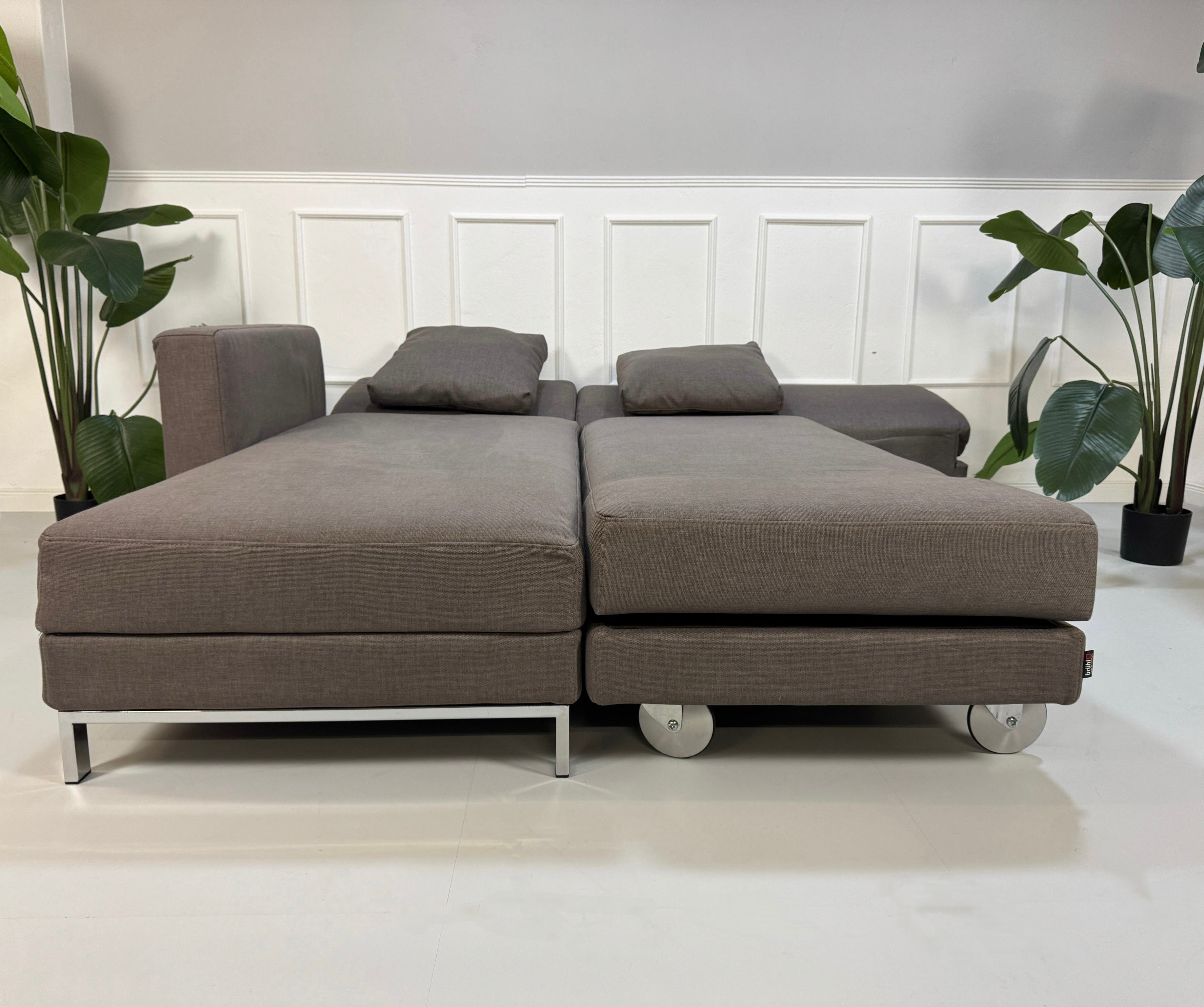 Gebrauchtes graues Brühl Fourtwo Designer Stoff Sofa vor einer Wand, stilvoll und modern eingerichtet.