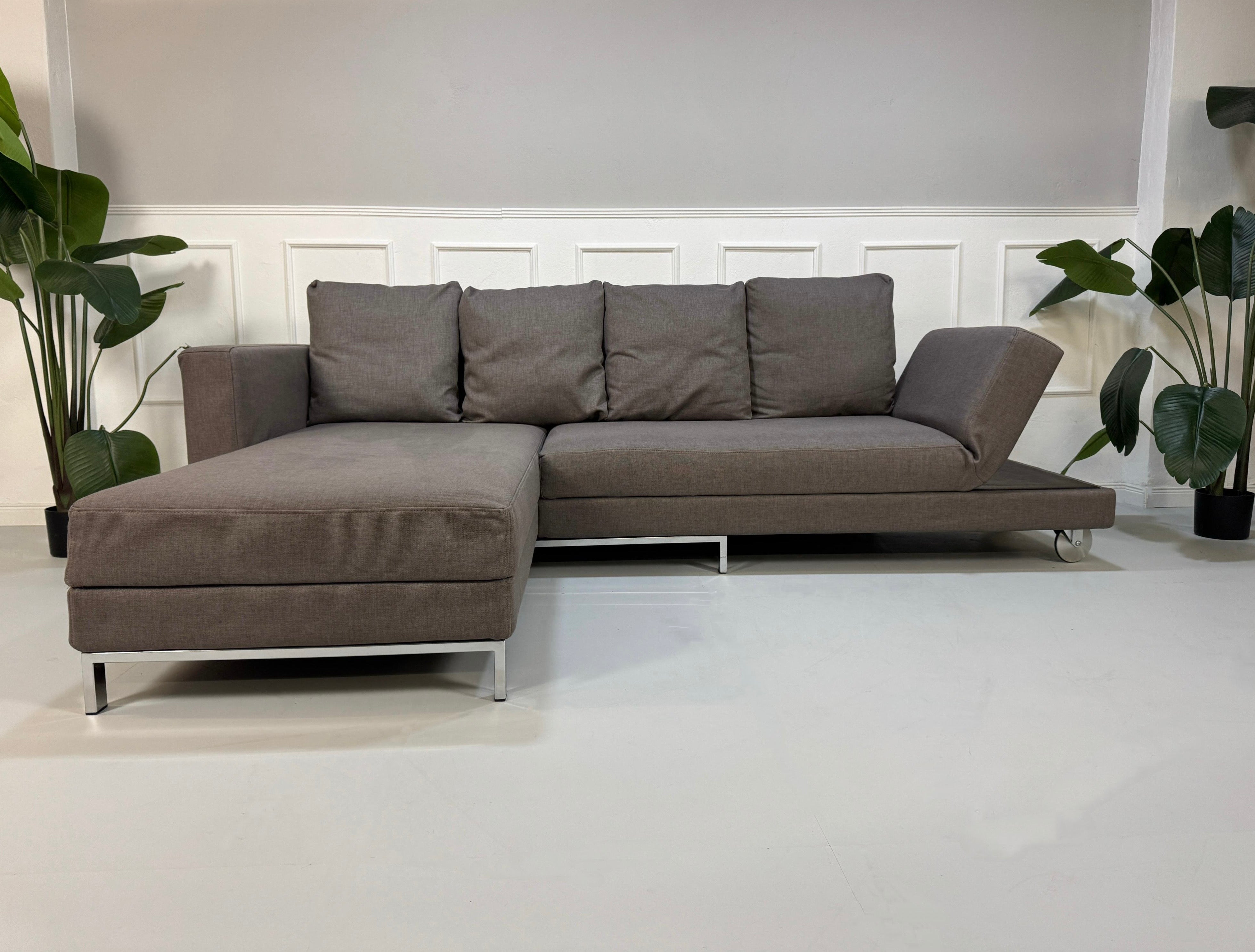 Gebrauchtes graues Brühl Fourtwo Designer Stoff Sofa vor einer Wand, stilvoll und modern eingerichtet.
