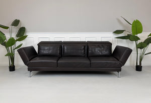 Gebrauchtes braunes Ledersofa Brühl Modell Moule 3 Sitzer vor einer modernen Wand.